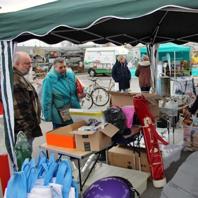 Menschen schauen unter einem Pavillon auf Tischen und in Kisten nach Büchern und Spielen.