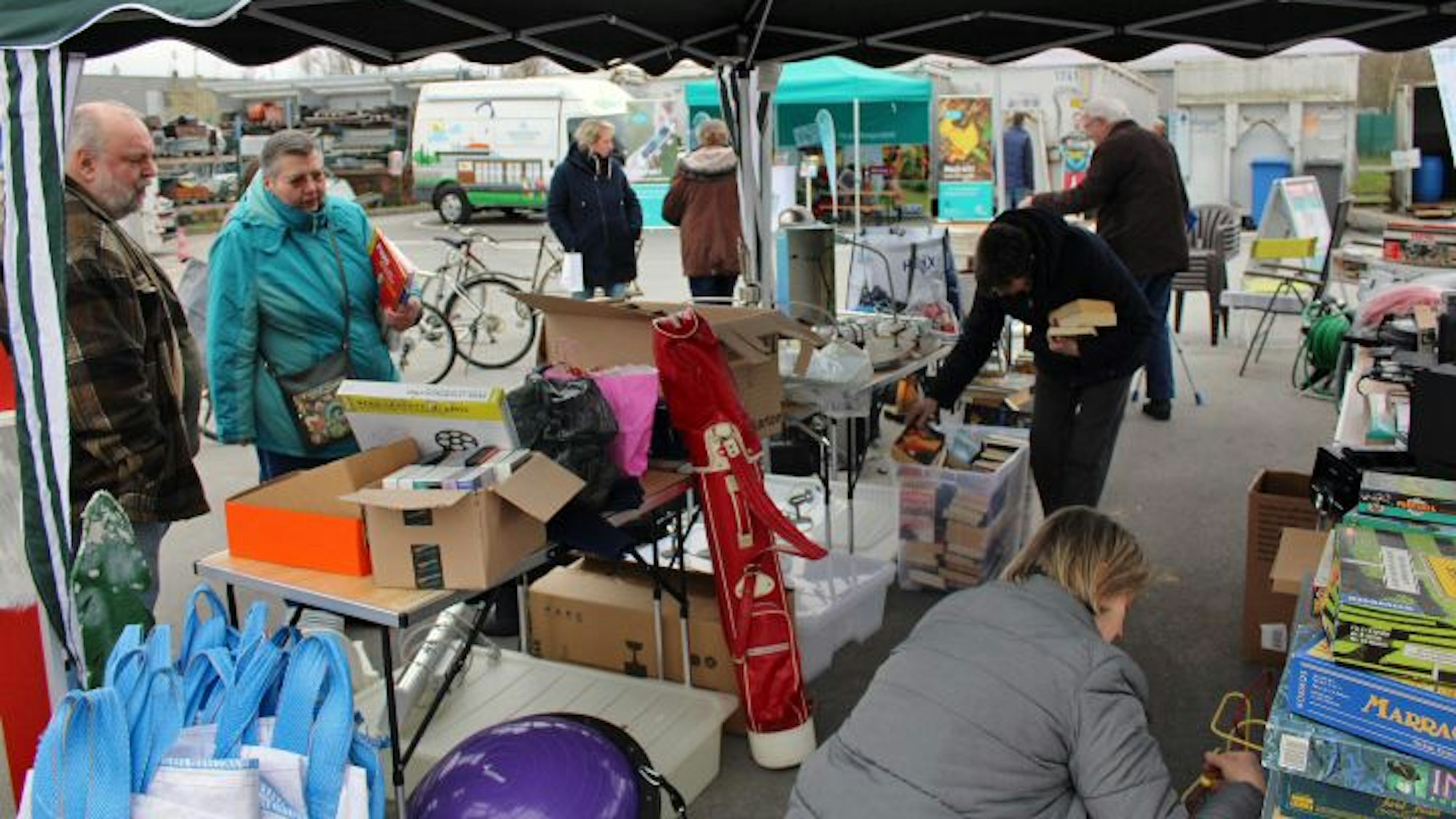 Menschen schauen unter einem Pavillon auf Tischen und in Kisten nach Büchern und Spielen.