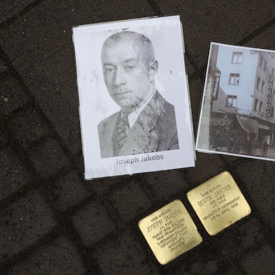 Neben zwei Stolpersteinen in Gedenken an Joseph und Berta Jakobs liegen zwei Bilder. Ein Porträt von Joseph und ein Bild von seinem Schuhgeschäft auf der Venloer Straße.