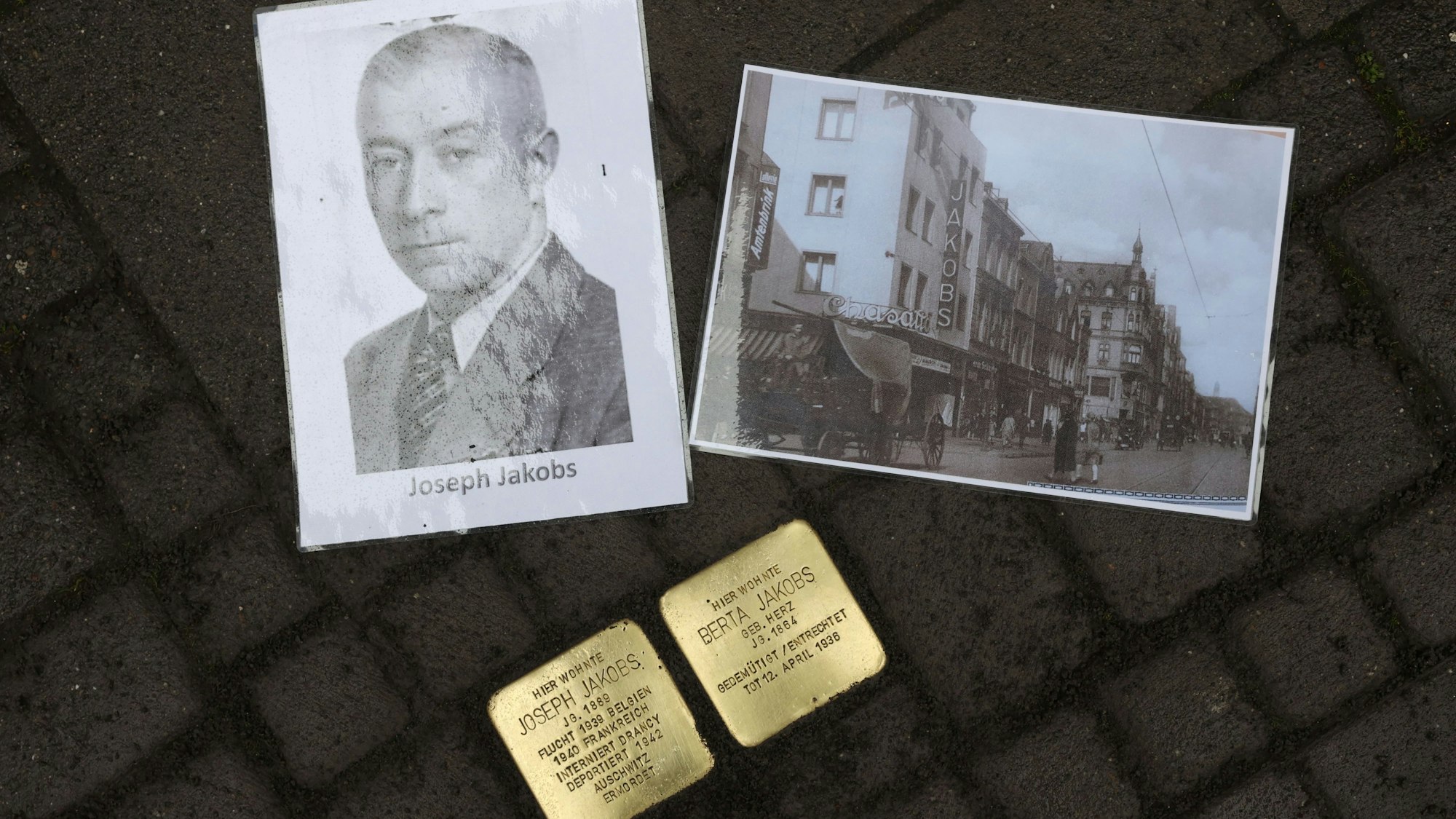 Neben zwei Stolpersteinen in Gedenken an Joseph und Berta Jakobs liegen zwei Bilder. Ein Porträt von Joseph und ein Bild von seinem Schuhgeschäft auf der Venloer Straße.