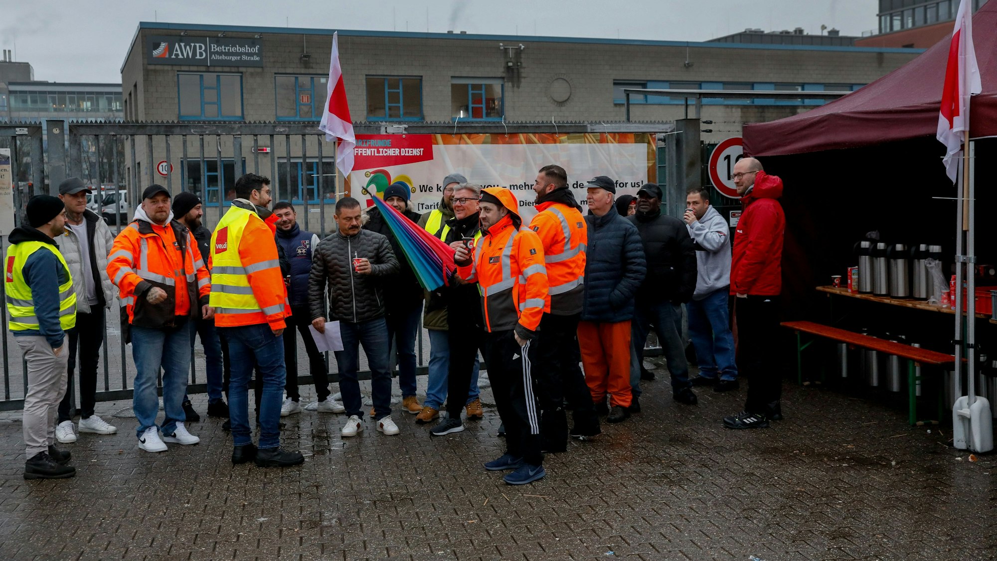 Männer in orangenen AWB-Jacken stehen vor dem Betriebshof der AWB. Manche tragen zusätzlich Warnwesten von Verdi.