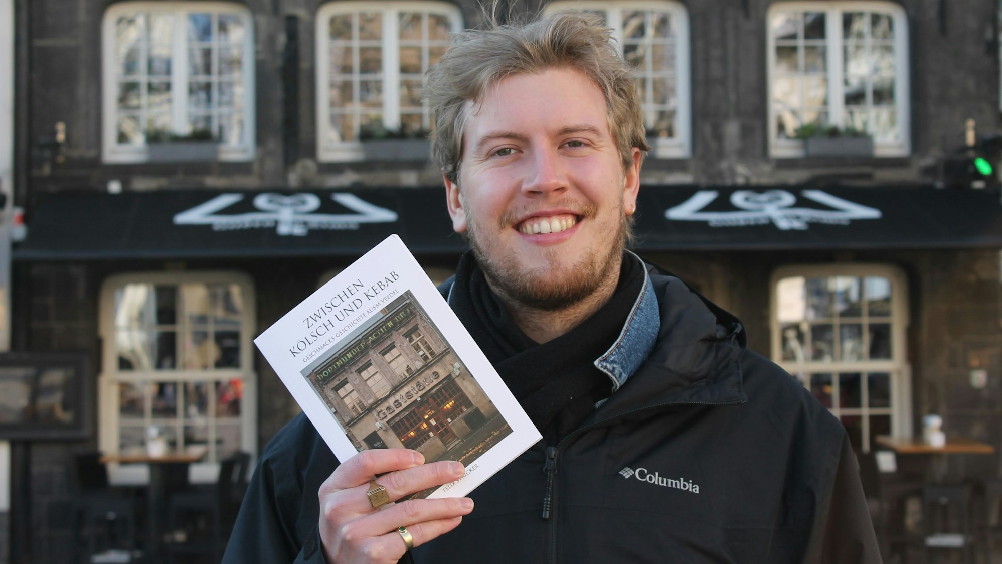 Ein Mann hält ein Buch in die Höhe mit dem Titel „Zwischen Kölsch und Kebab“.