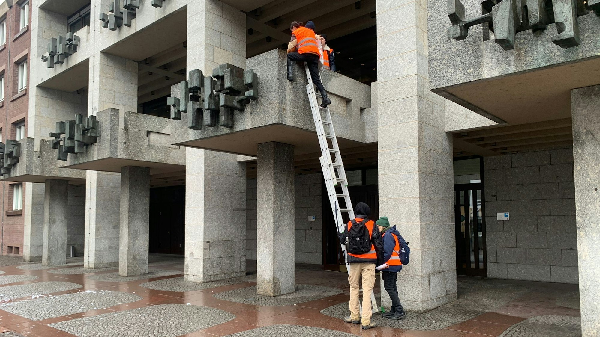 Mehrere Aktivisten halten eine Leiter. Einer klettert auf den Balkon.