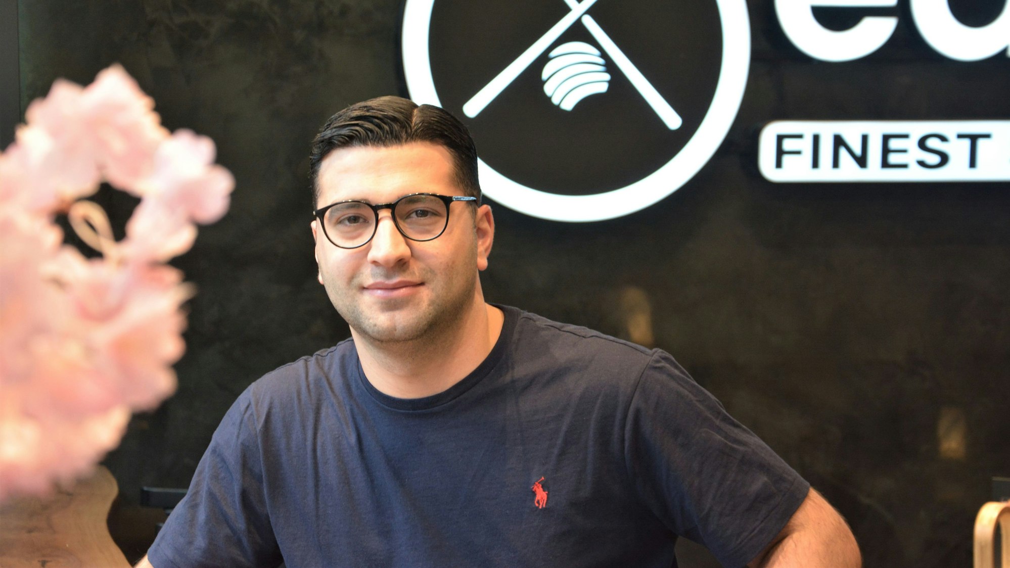 Said Altintas im blauen T-Shirt vor einer Wand mit dem Logo seines Sushi-Restaurants.