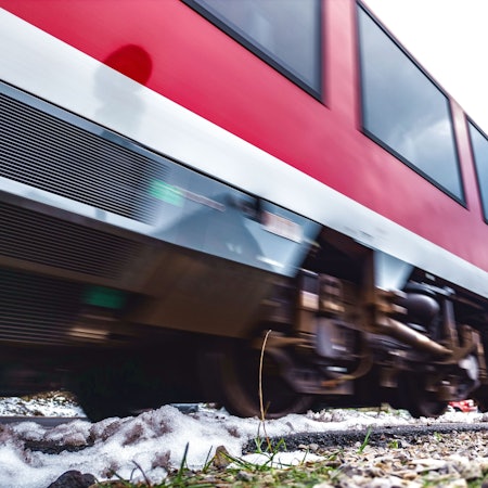 Ein rot-weißer Regionalzug rauscht über Bahnschienen.