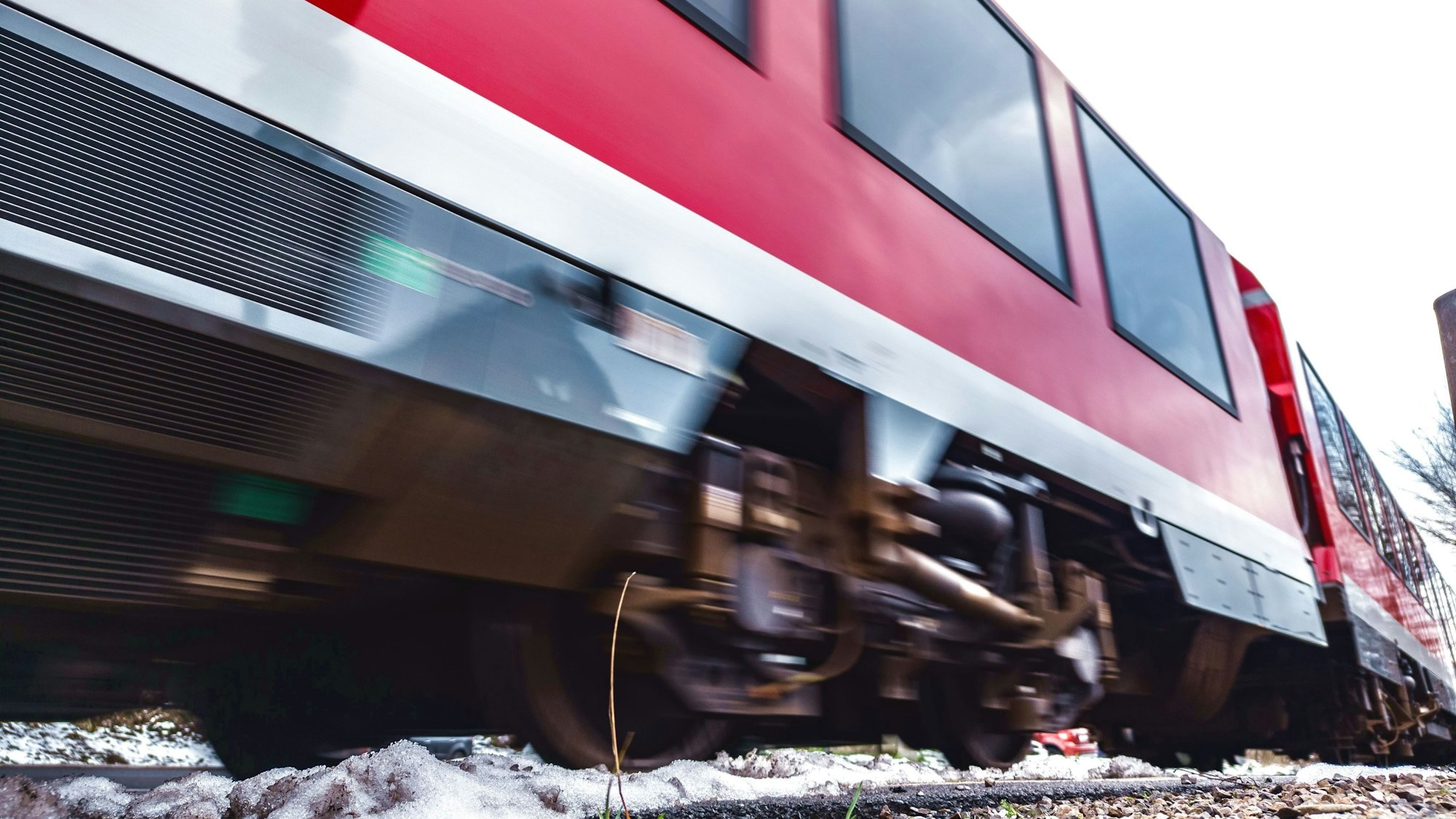 Ein rot-weißer Regionalzug rauscht über Bahnschienen.