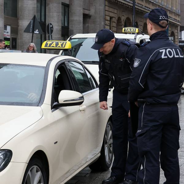 Zöllner sprechen mit einem Taxifahrer, der im Auto sitzt.