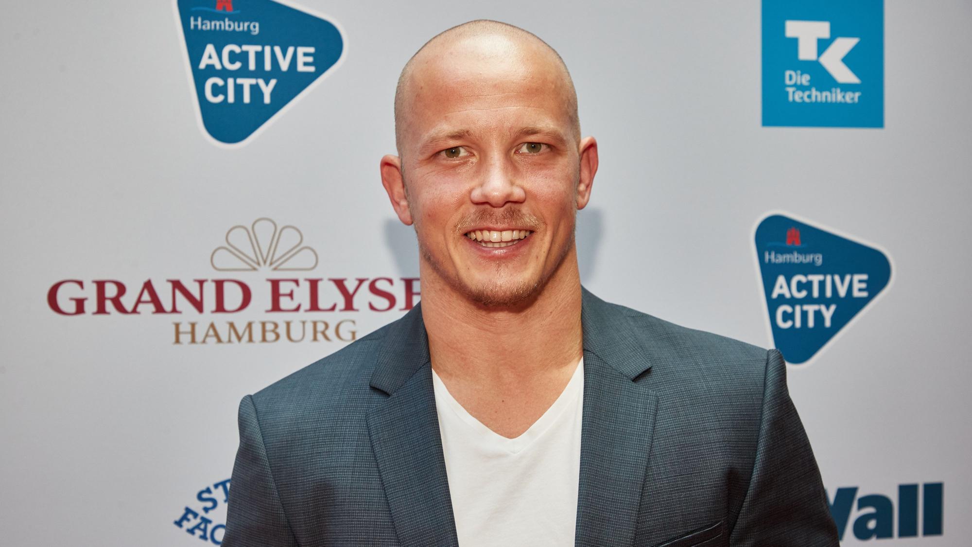 Fabian Hambüchen steht vor einer Wand, auf der die Sponsoren des Deutschen Sportjournalistenpreises zu sehen sind.