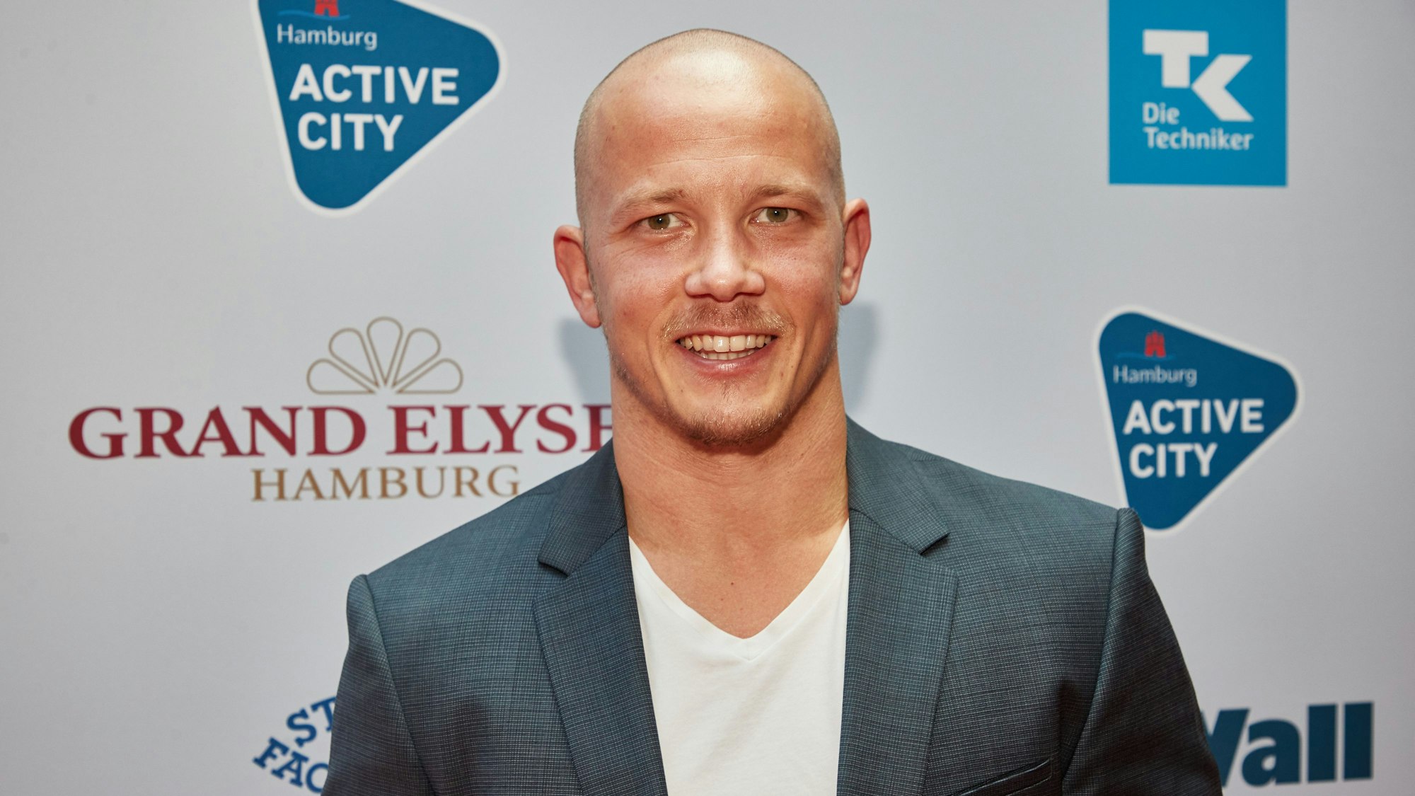 Fabian Hambüchen steht vor einer Wand, auf der die Sponsoren des Deutschen Sportjournalistenpreises zu sehen sind.