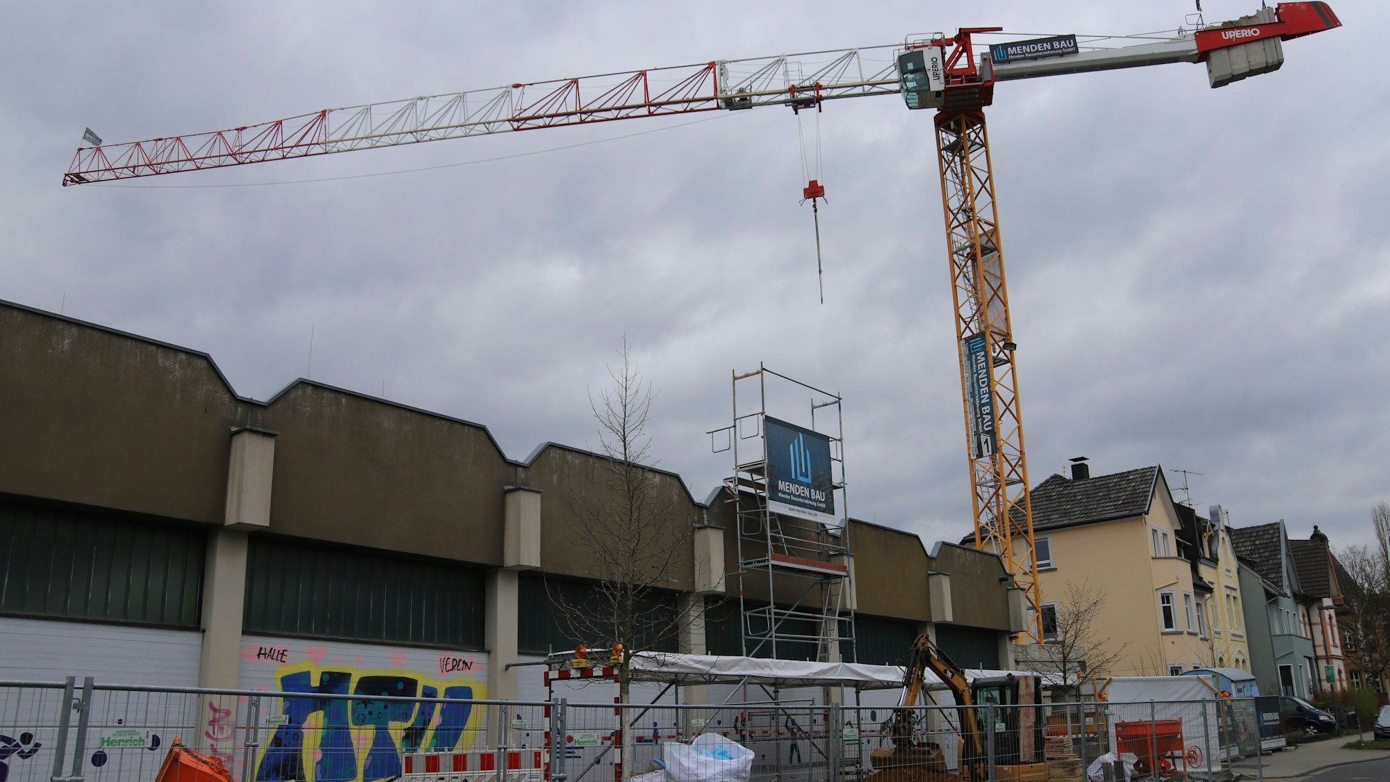 Ein Baukran hievt einen Bagger über die Fritz-Kuchenmeister-Halle.