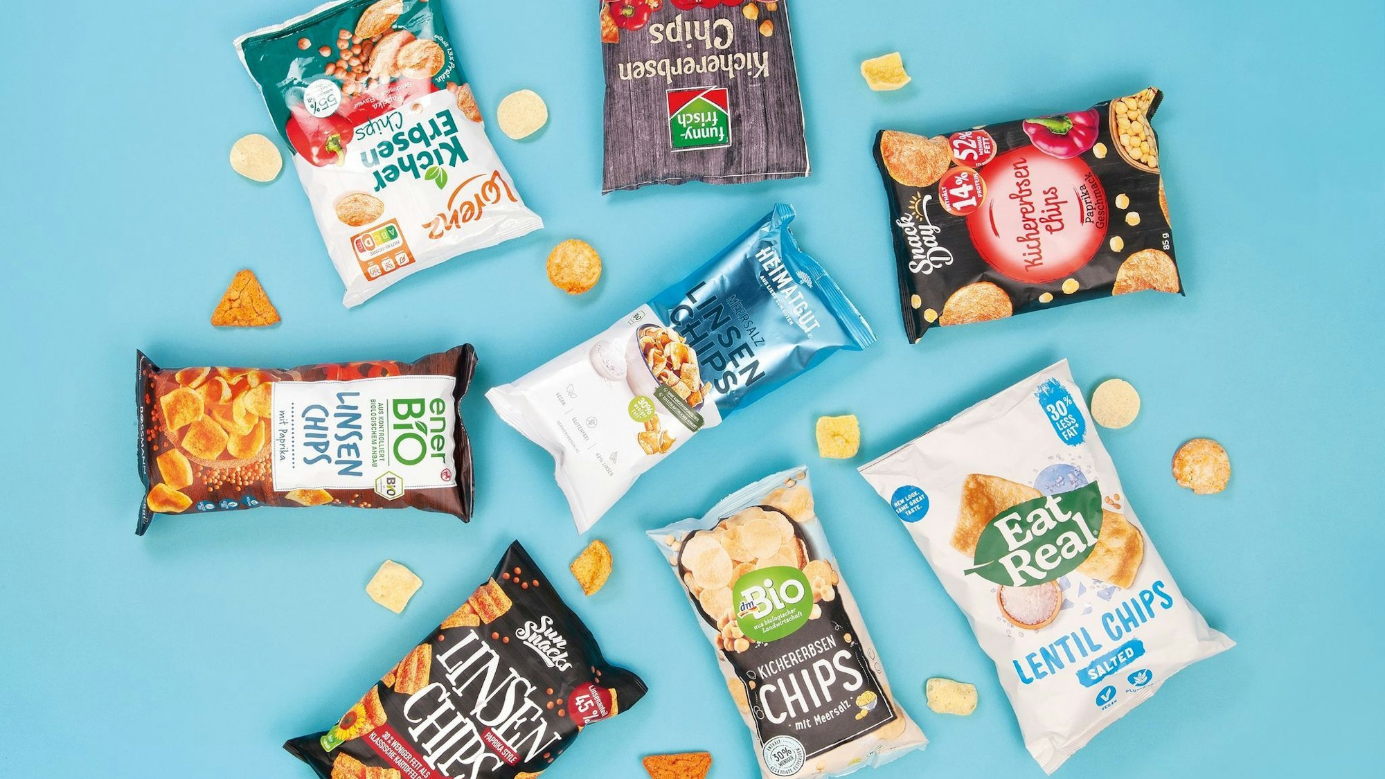 Acht Chipstüten liegen auf einem hellblauen Boden.