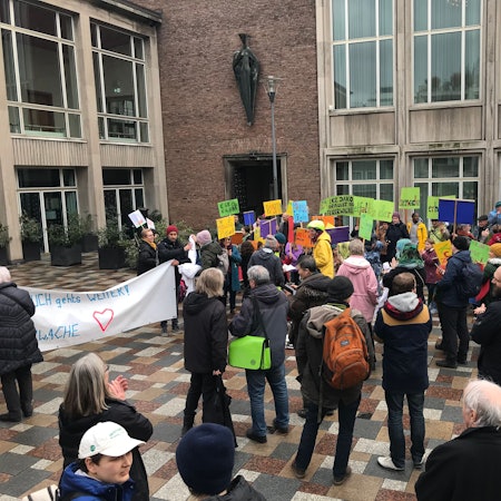 Menschen stehen mit bunten Plakaten vor dem Kölner Rathaus.