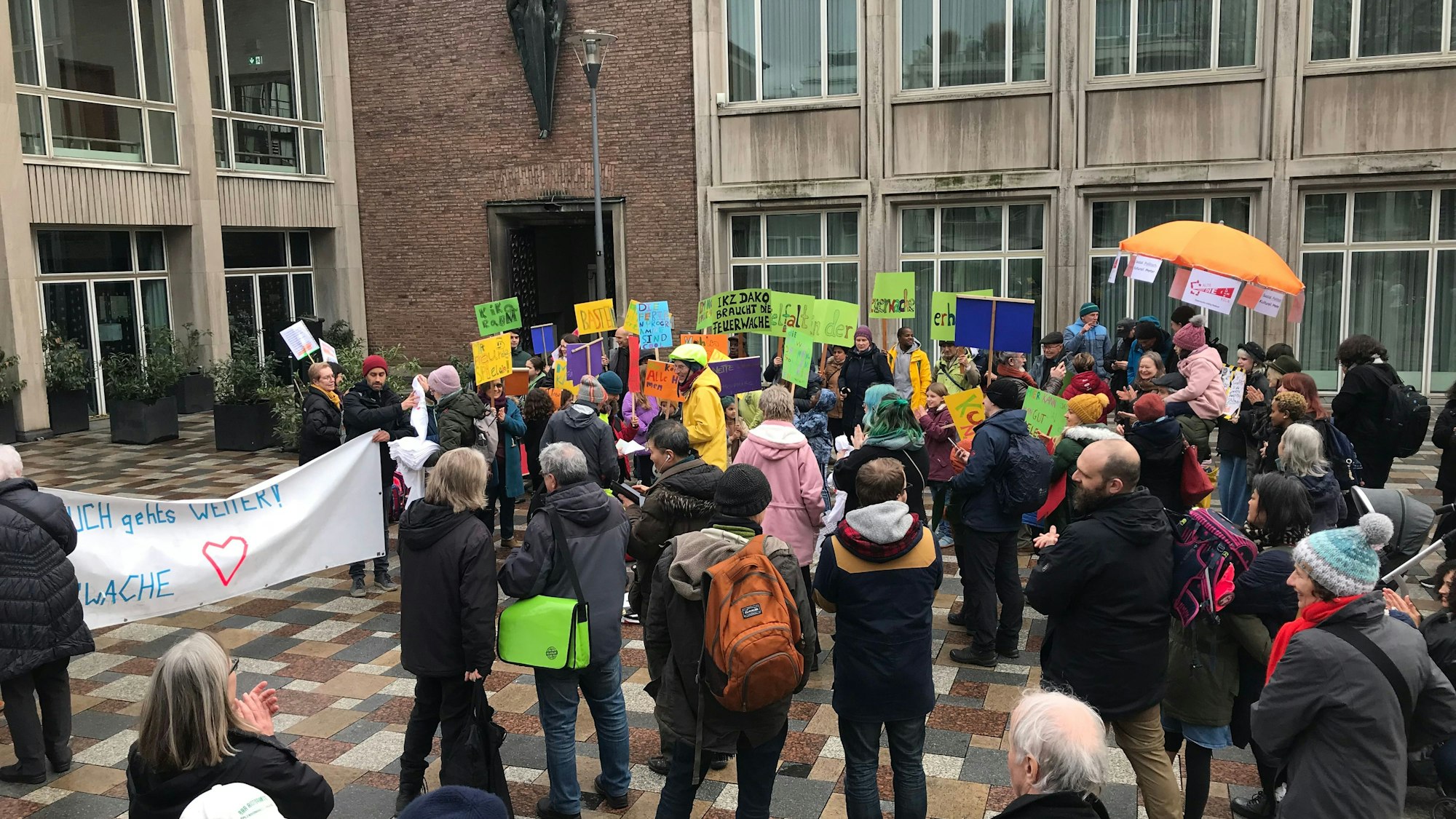 Menschen stehen mit bunten Plakaten vor dem Kölner Rathaus.