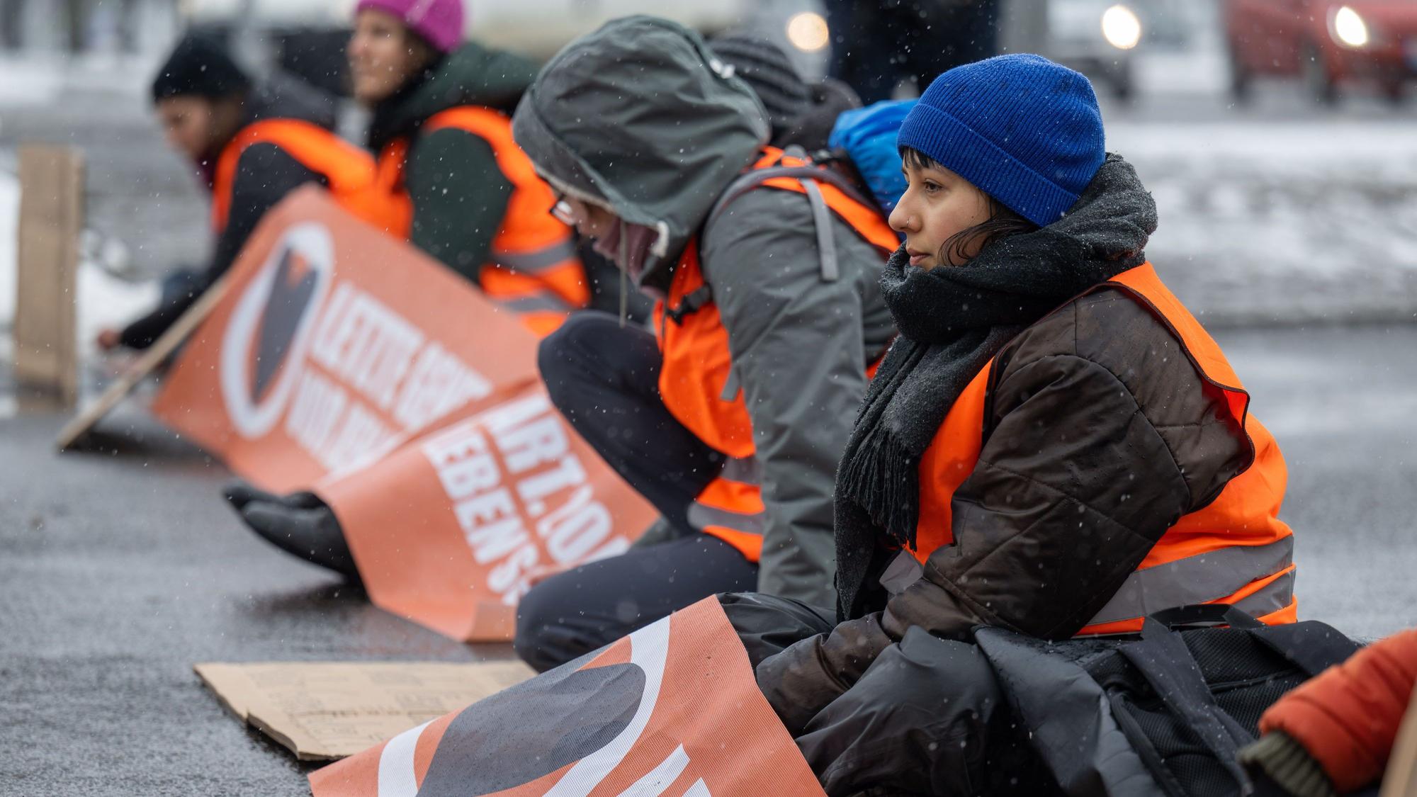 08.03.2023, Sachsen, Leipzig: Aktivistinnen der Letzten Generation haben sich auf der Fahrbahn der Jahnallee in Leipzig festgeklebt. Mit Bannern und Plakaten haben die Aktivistinnen den Verkehr in Fahrtrichtung Innenstadt aufgehalten.