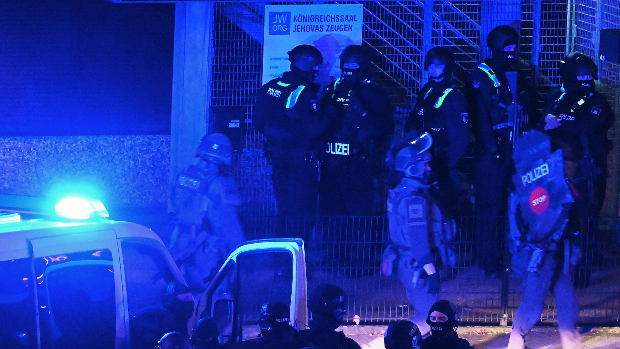 Polizisten sind in Hamburg im Einsatz und stehen vor einem Schild mit der Aufschrift Königreichssaal „Jehovas Zeugen“.