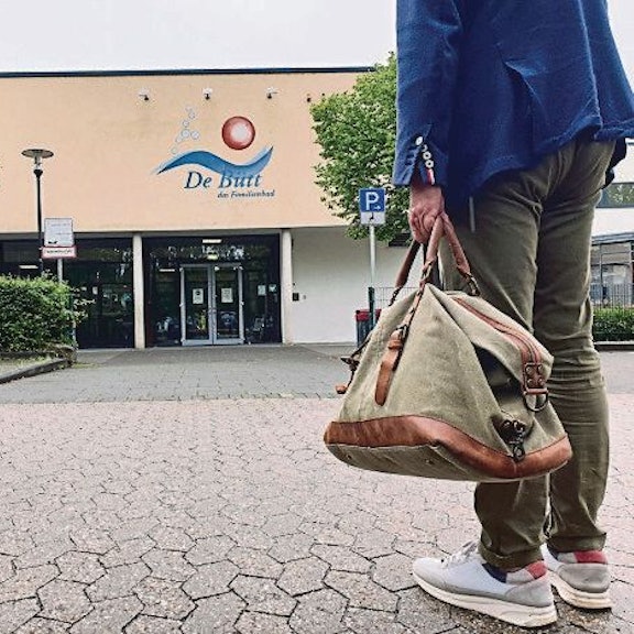 Das Foto zeigt einen Mann mit einer Sporttasche, der in Richtung des Familienbads De Bütt geht.