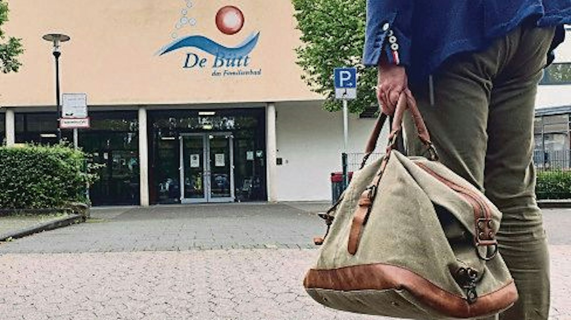 Das Foto zeigt einen Mann mit einer Sporttasche, der in Richtung des Familienbads De Bütt geht.