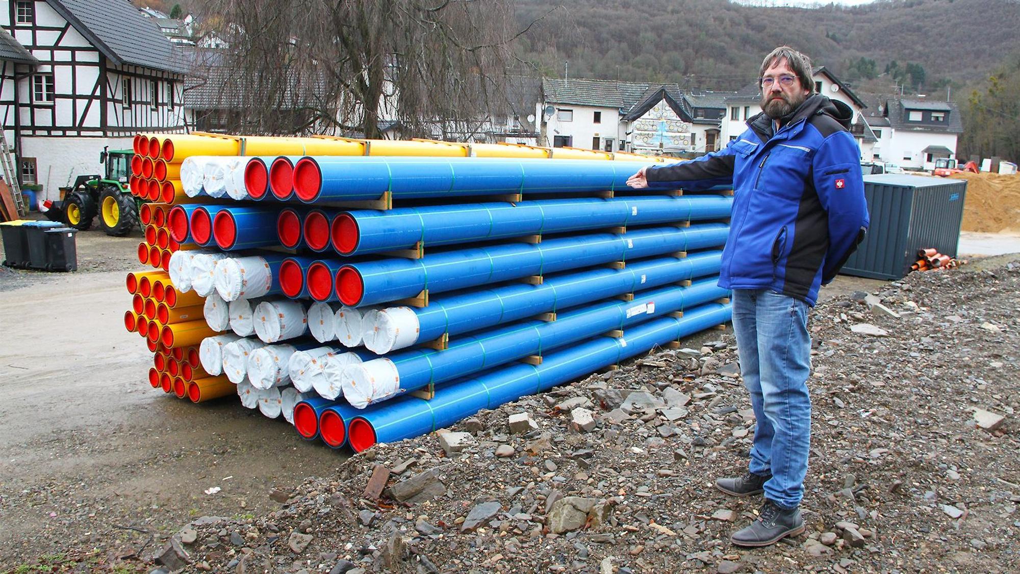 Ein Mann steht vor einem Stapel blauer und gelber Rohre.