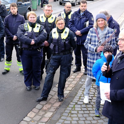 Polizistinnen und Polizisten sowie Menschen in ziviler Kleidung stehen auf einer Straße und hören Michael Heinen zu.