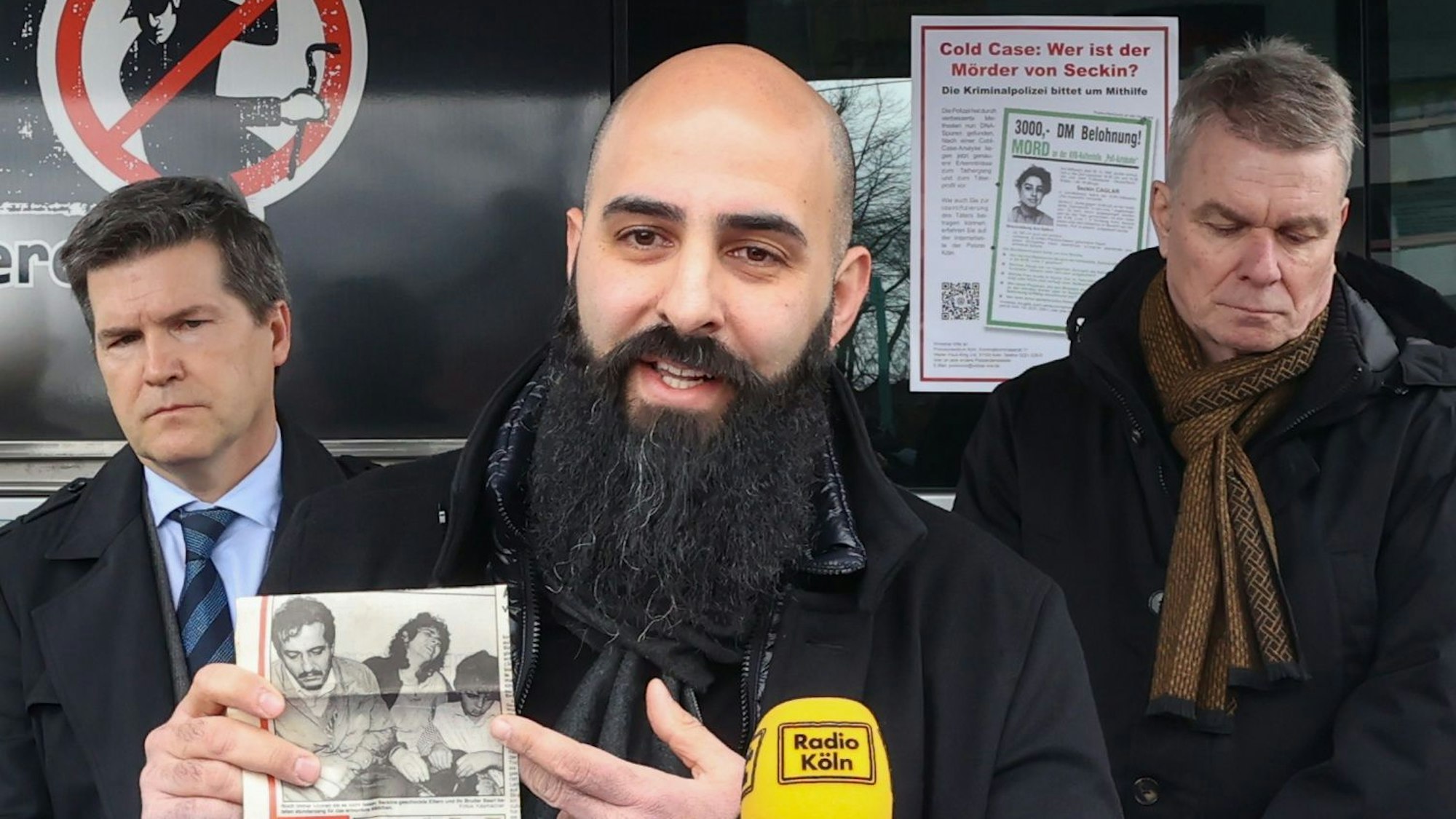 Basri Caglar, der Bruder der 1991 ermordeten Seckin, zeigt auf dem Poller Marktplatz einen alten Zeitungsartikel über die Tat – neben ihm Oberstaatsanwalt Ulrich Bremer (l.) und Hauptkommissar Markus Weber (r.).