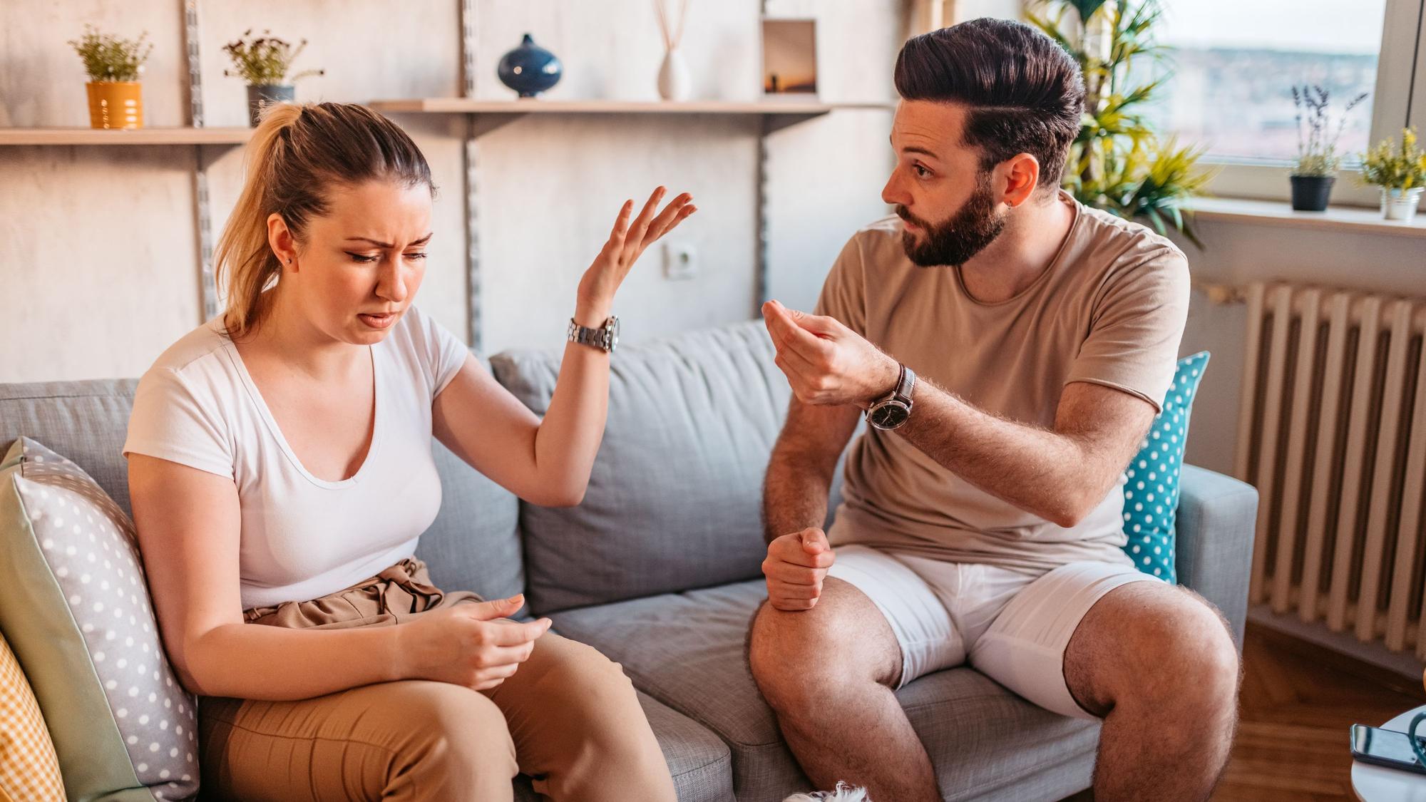 Ein Mann und eine Frau sitzen auf einem Sofa. Der Mann möchte diskutieren, die Frau wnkt genervt ab