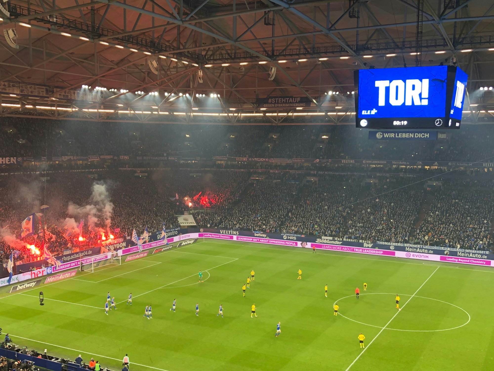 In der Fankurve der Schalker brennen bengalische Feuer. Auf dem großen Videowürfel über dem Spielfeld steht: Tor!