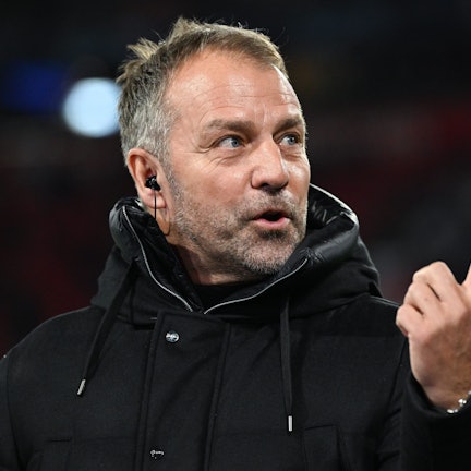 Bundestrainer Hansi Flick steht in einer schwarzen Jacke am Spielfeldrand, er hebt den Zeigefinger.