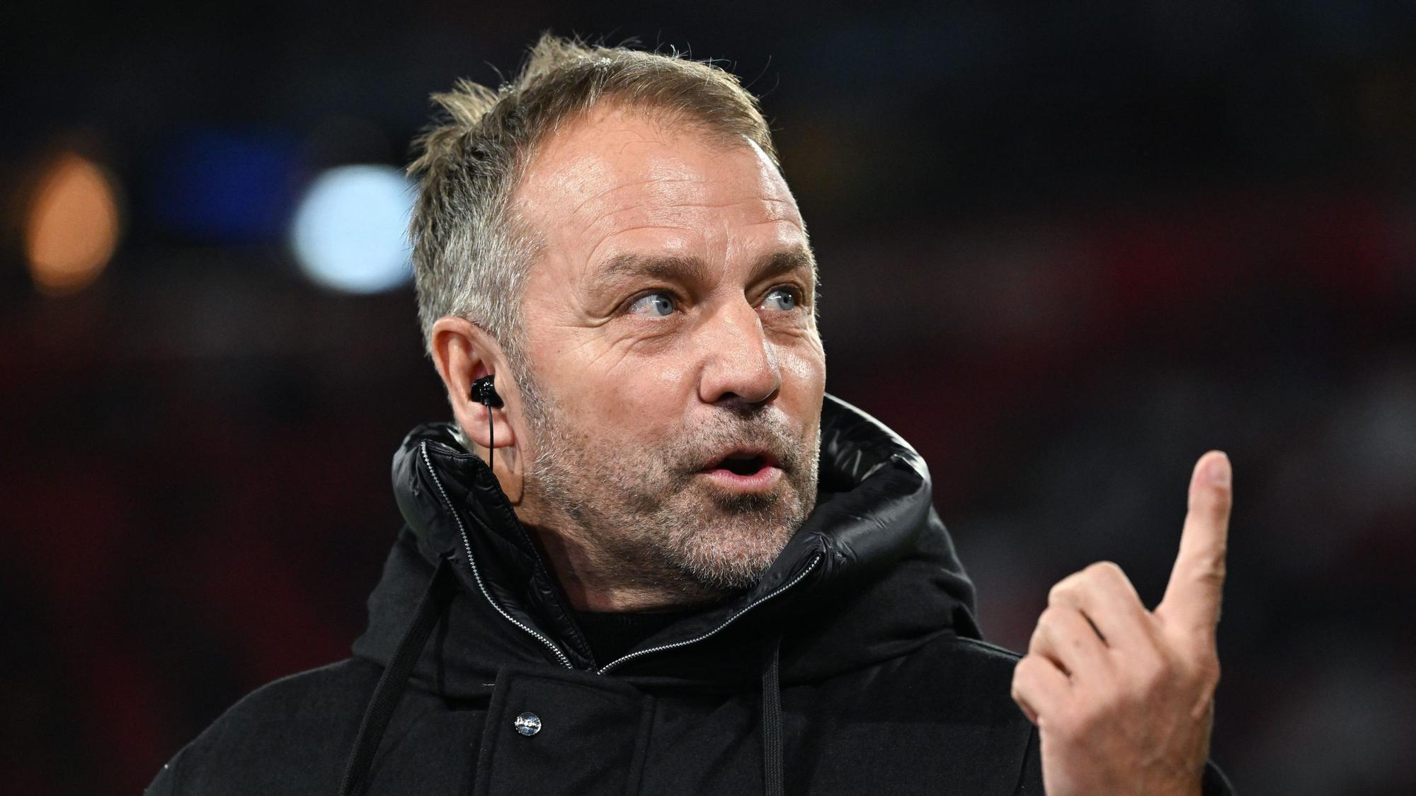 Bundestrainer Hansi Flick steht in einer schwarzen Jacke am Spielfeldrand, er hebt den Zeigefinger.
