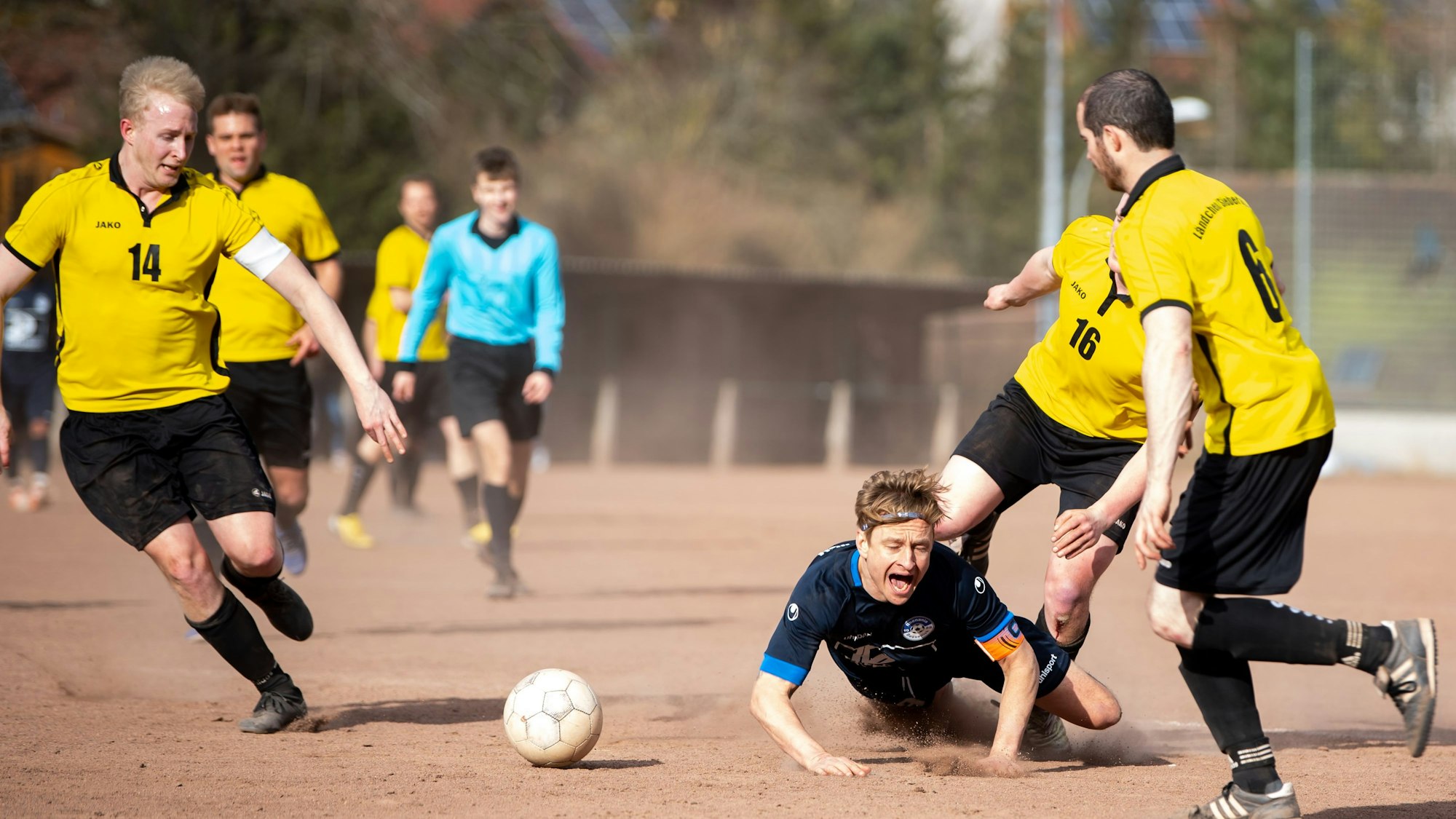 Ein Fußballer fällt nach einem Zweikampf auf die Asche.