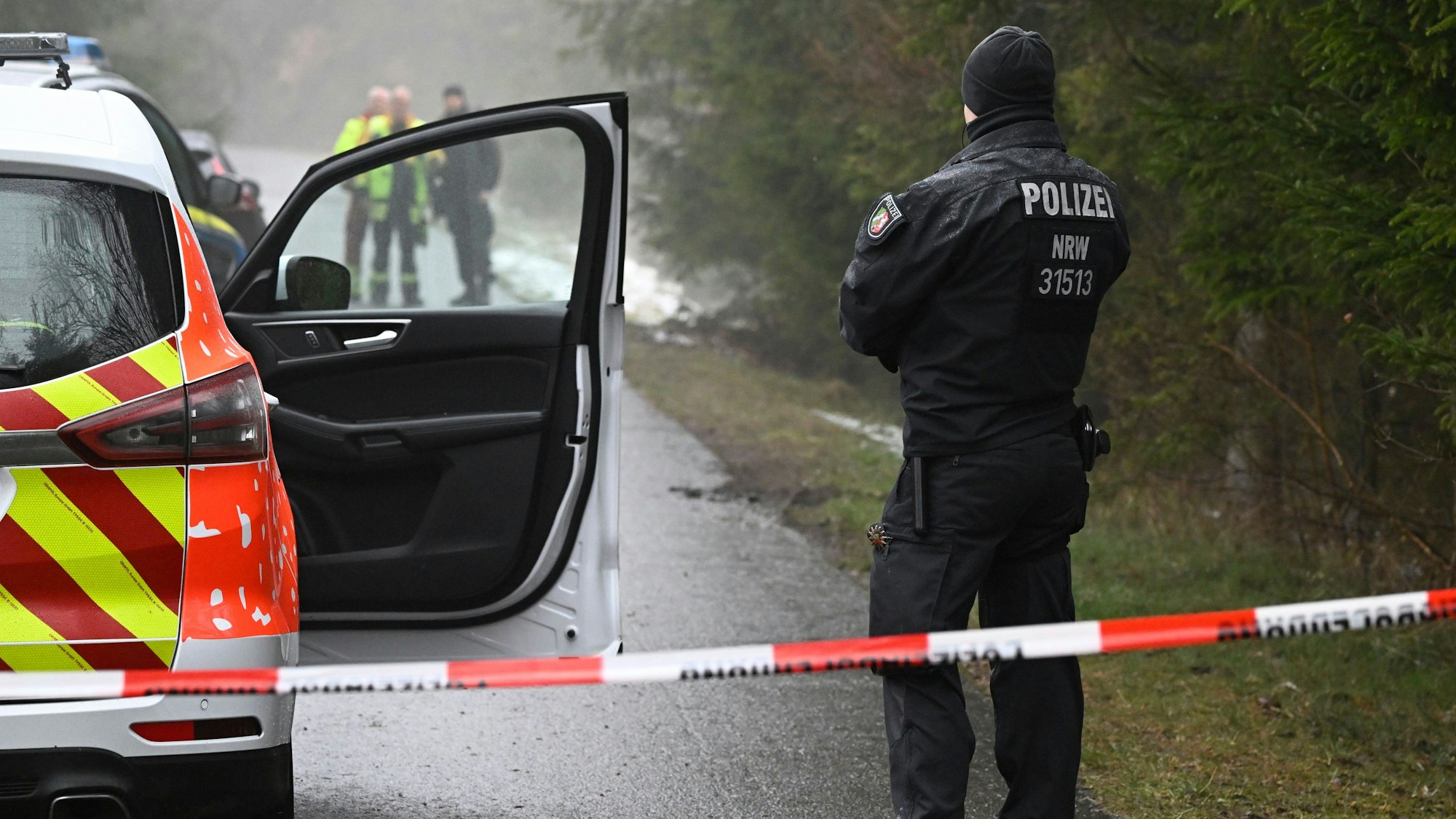 Einsatzkräfte der Polizei stehen nahe des Fundorts einer Leiche in Freudenberg an einer Absperrung.