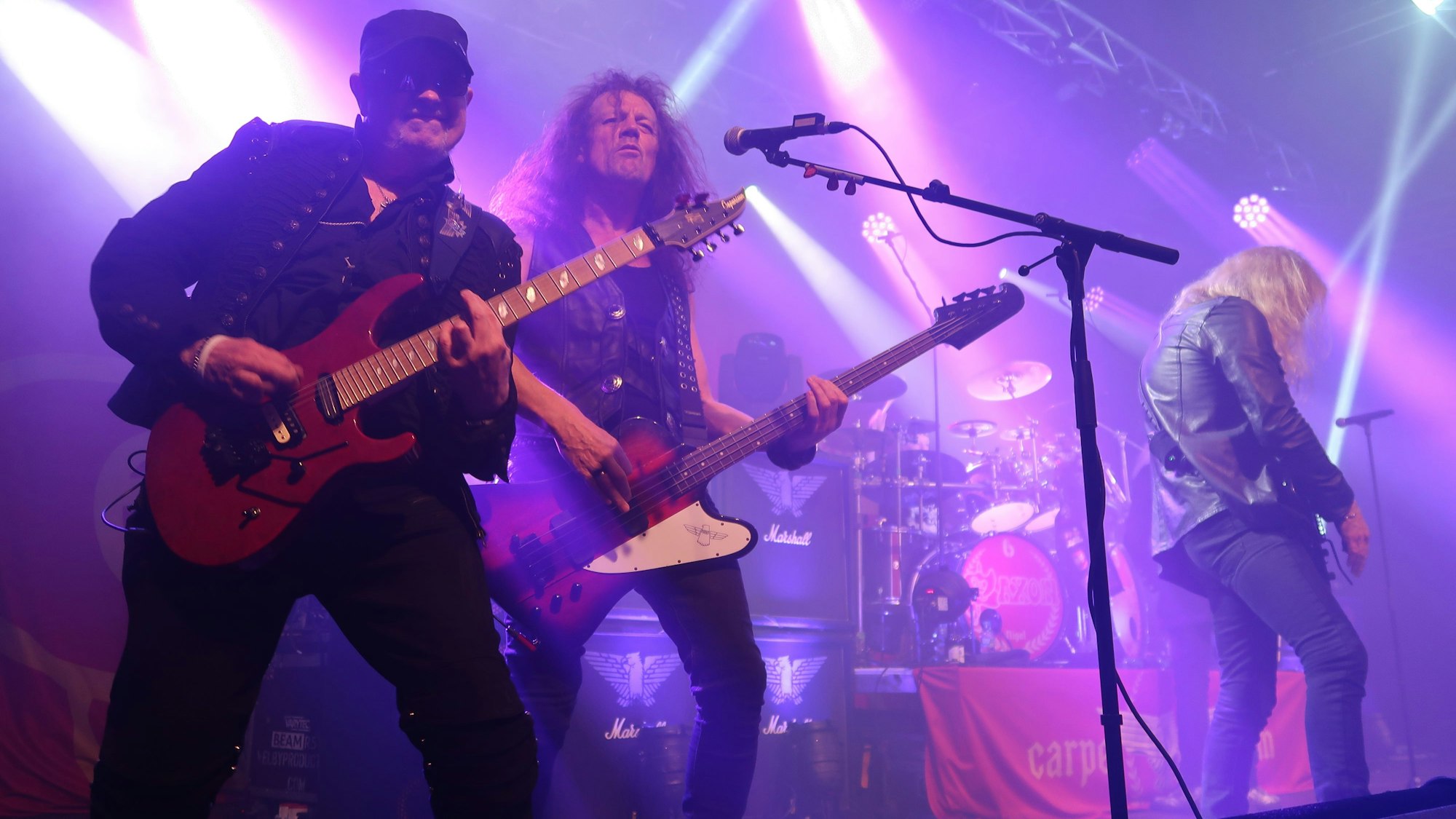 Ein Gitarrist und ein Musiker posieren auf einer in violettes Licht getauchten Bühne für den Fotografen.