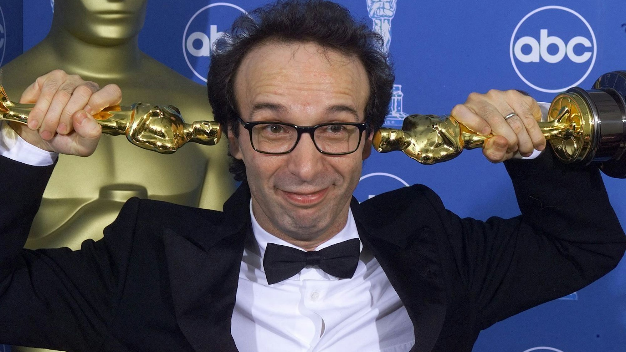 Roberto Benigni mit zwei Oscars neben den Ohren, links und rechts.