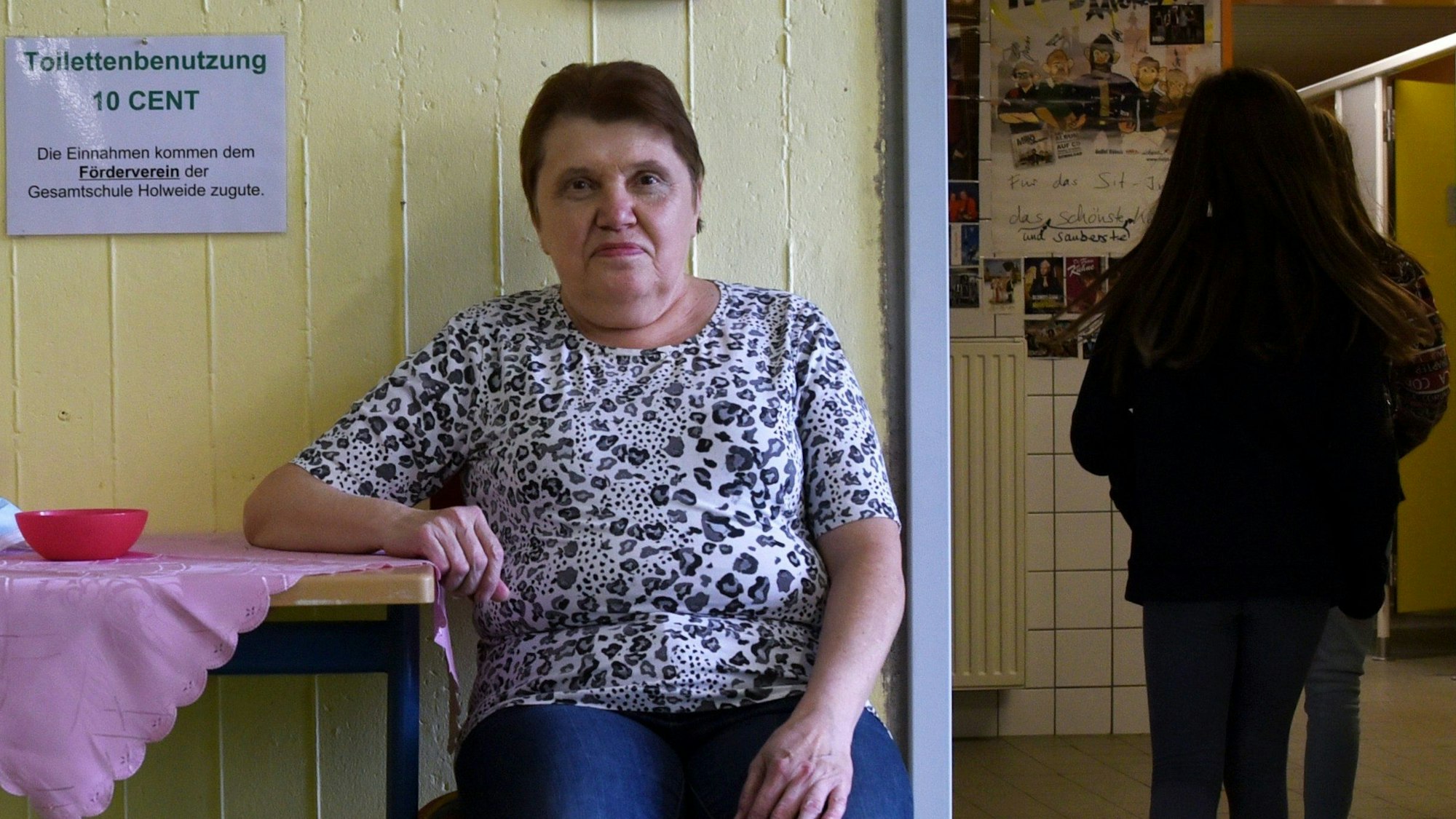 Eine Frau sitzt an einem Tischchen vor einer Toilettenanlage.