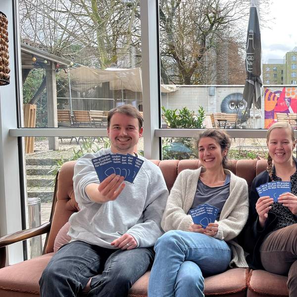 Drei junge Menschen halten Flyer in die Kamera.