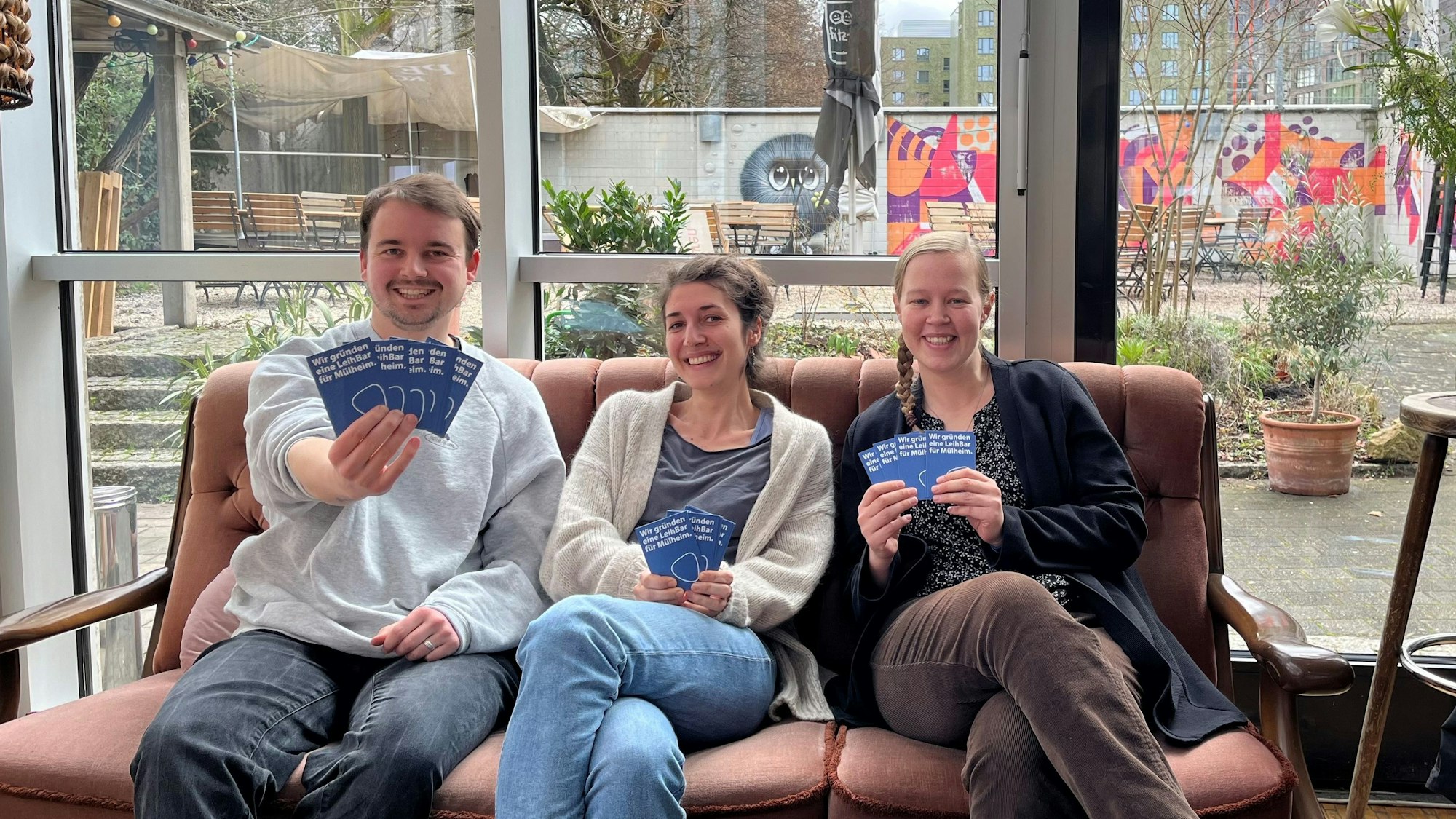 Drei junge Menschen halten Flyer in die Kamera.