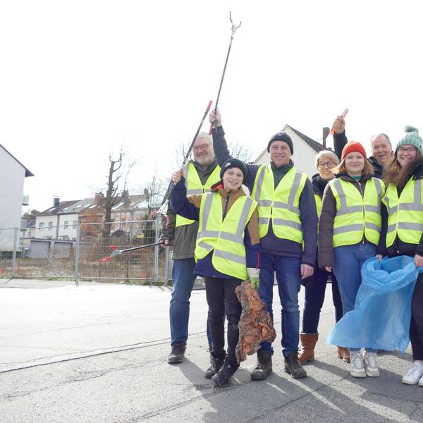 Eine Gruppe Frauen, Männer und Kinder in gelben Warnwesten und mit Mülltüten schwenken ihre Greifzangen.