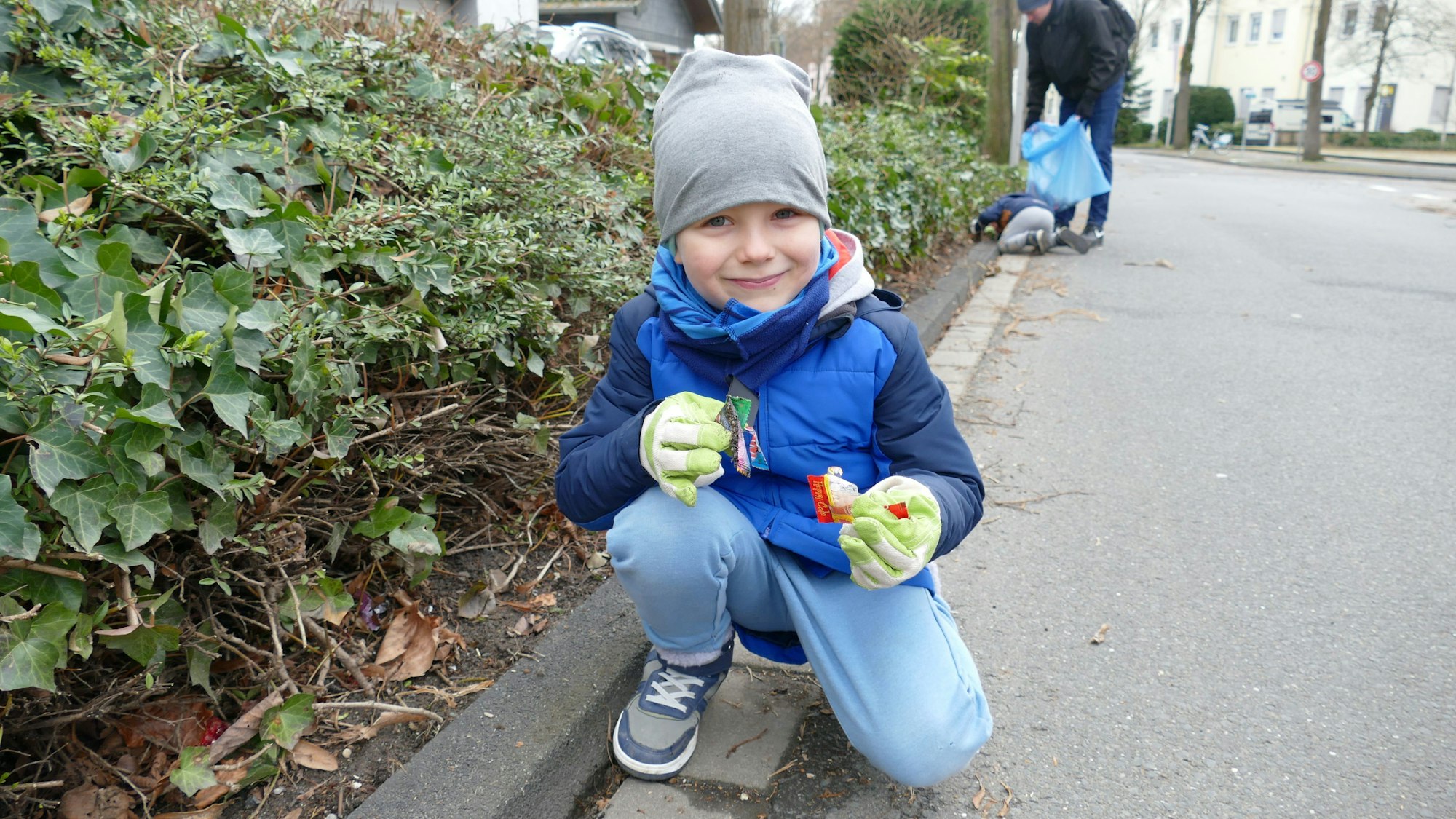 Ein Junge kniet im Rinnstein und hält Bonbontütchen in seinen behandschuhten Händen.