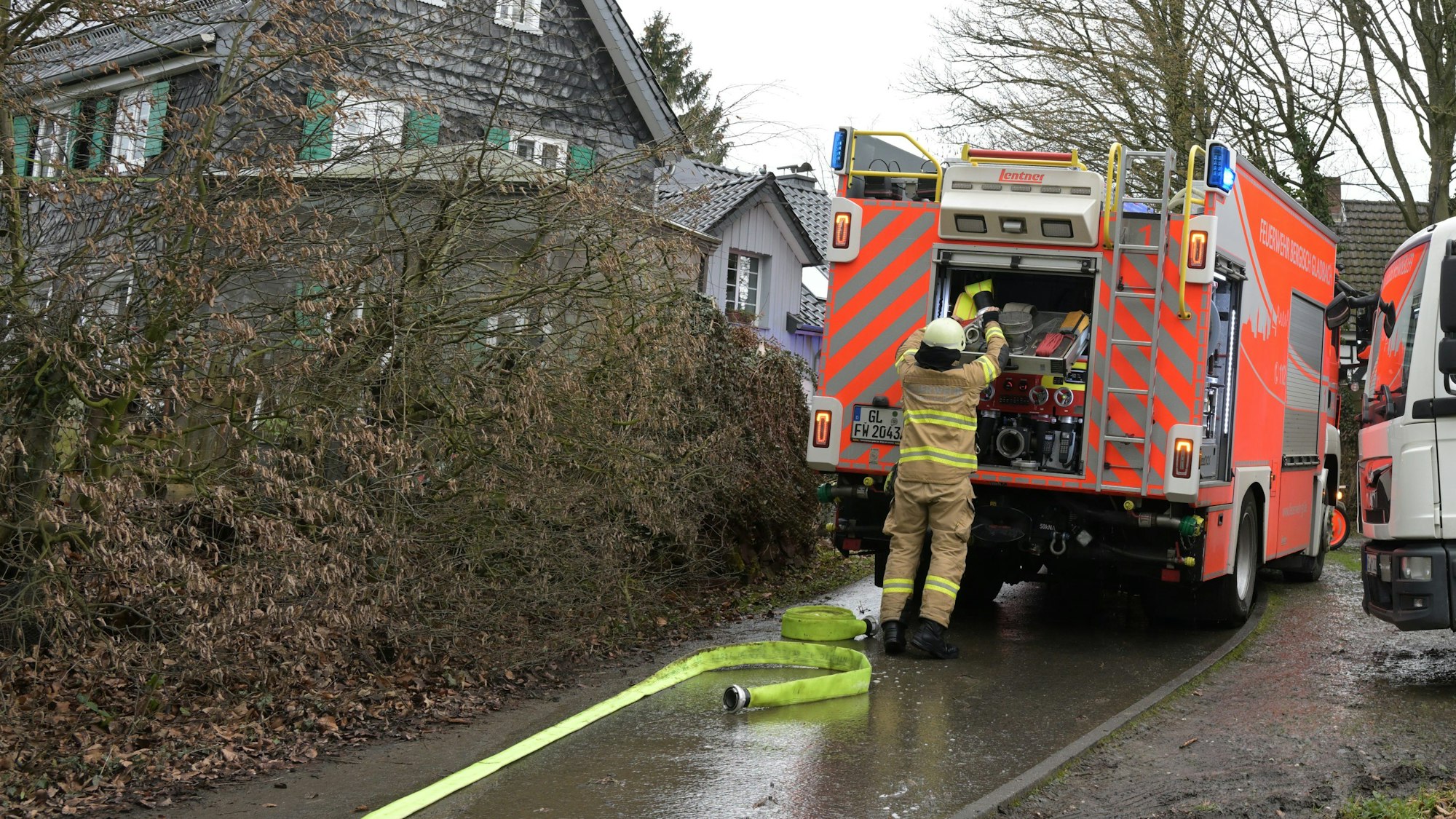 Ein Feuerwehrmann lädt Material in ein Feuerwehrfahrzeug. Im Hintergrund sind mehrere Gebäude zu sehen.