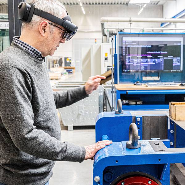Ein Mann steht an einem Arbeitsplatz in einer Fabrikhalle. Er trägt eine Datenbrille.
