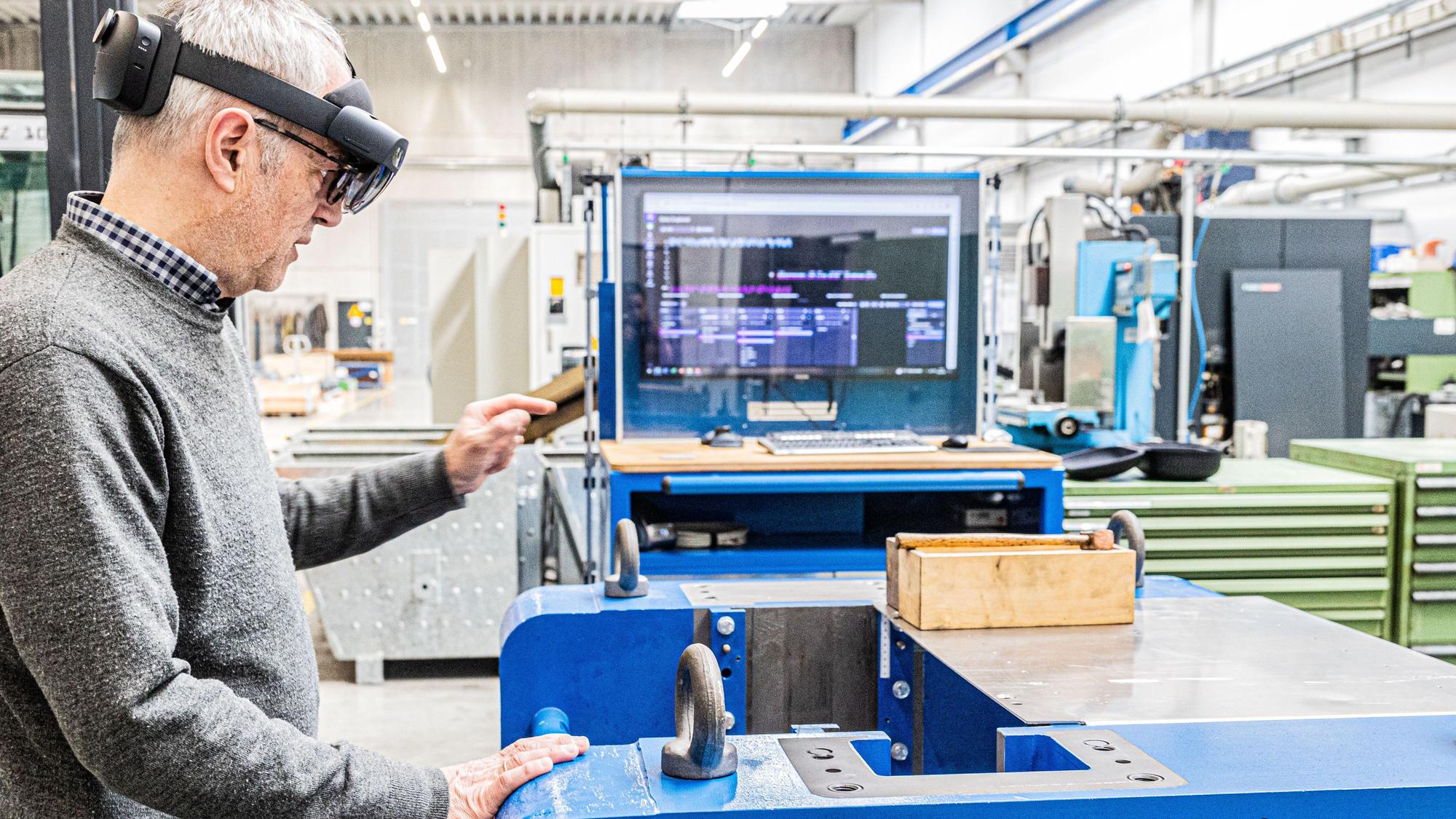 Ein Mann steht an einem Arbeitsplatz in einer Fabrikhalle. Er trägt eine Datenbrille.
