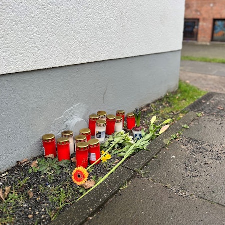 Blumen und Kerzen liegen einen Tag nach dem Tötungsdelikt an einem 23-jährigen Mann auf dem Gehweg der Moses-Heß-Straße in Köln-Stammheim