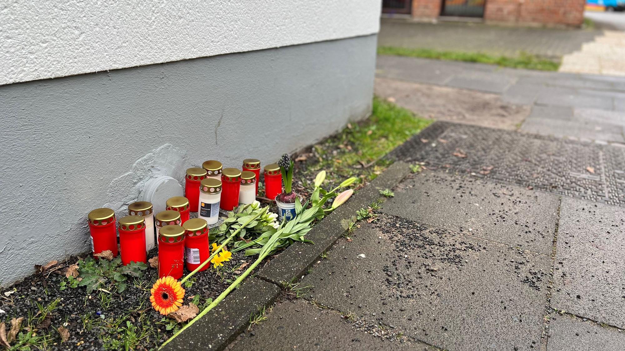 Blumen und Kerzen liegen einen Tag nach dem Tötungsdelikt an einem 23-jährigen Mann auf dem Gehweg der Moses-Heß-Straße in Köln-Stammheim