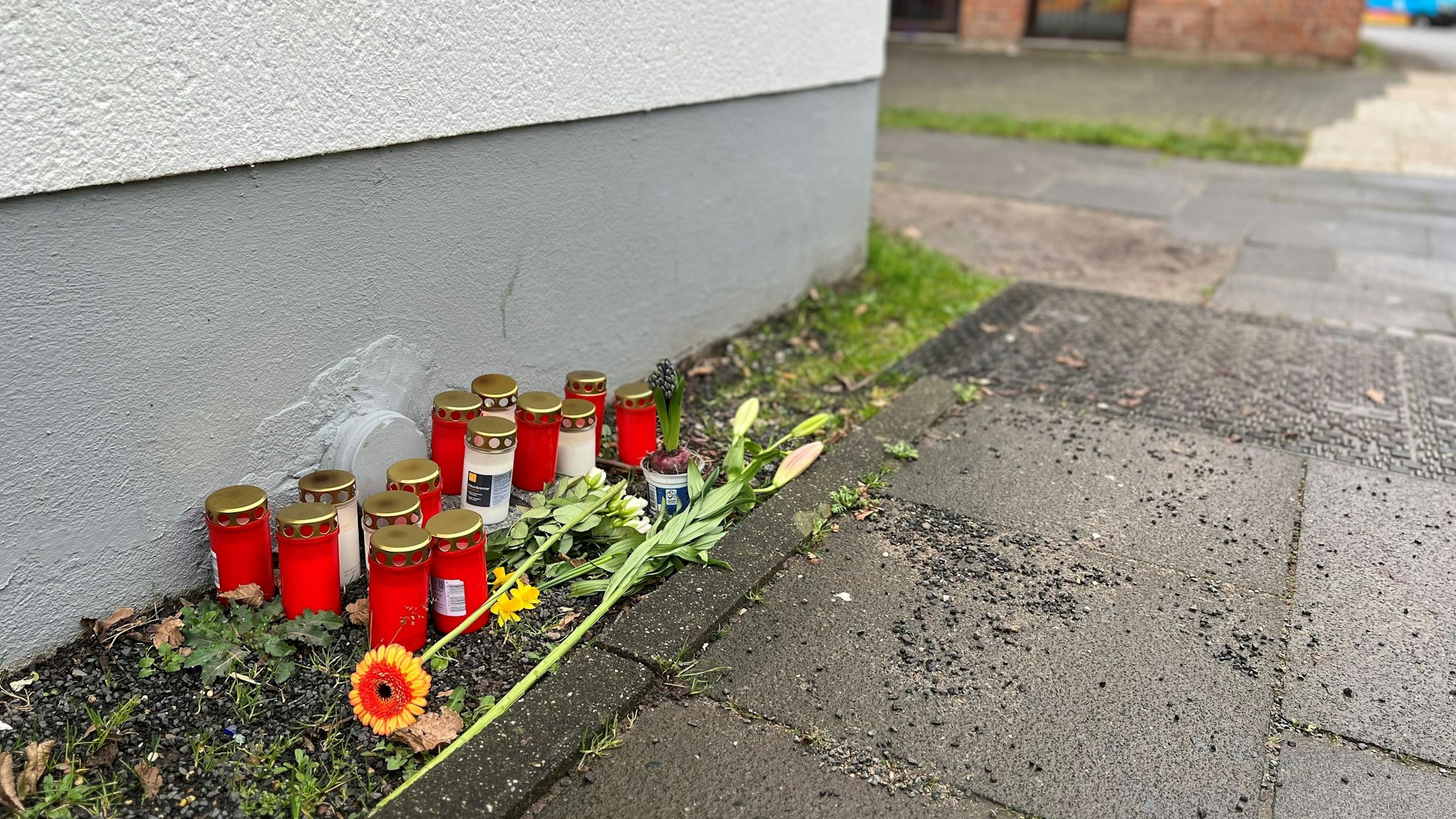 Blumen und Kerzen liegen einen Tag nach dem Tötungsdelikt an einem 23-jährigen Mann auf dem Gehweg der Moses-Heß-Straße in Köln-Stammheim