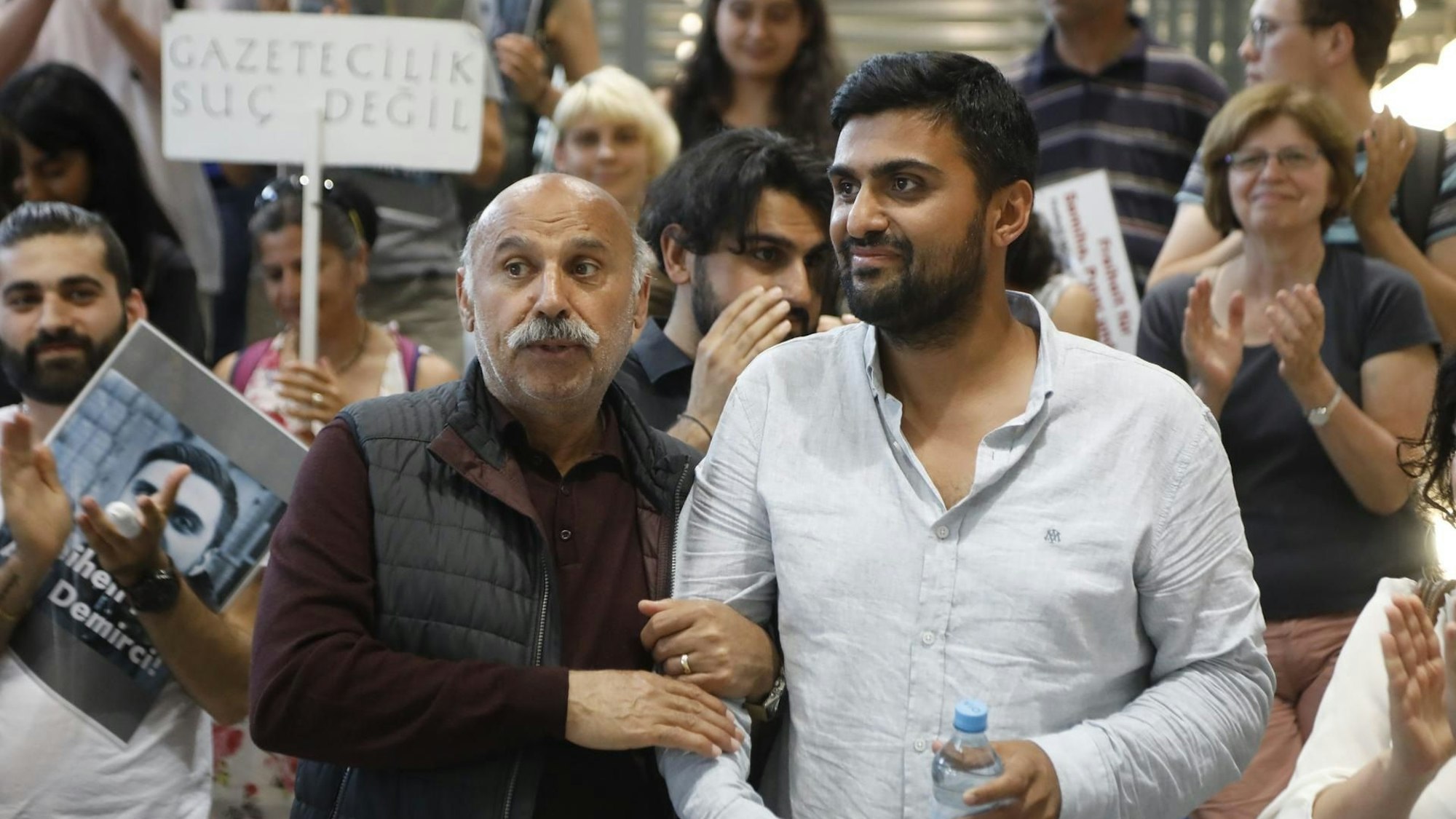 Adil Demirci und sein Vater nach Demircis Rückkehr nach Köln. Im Hintergrund Menschen mit Plakaten, die für die Freilassung des Kölners aus türkischer Haft demonstriert hatten.