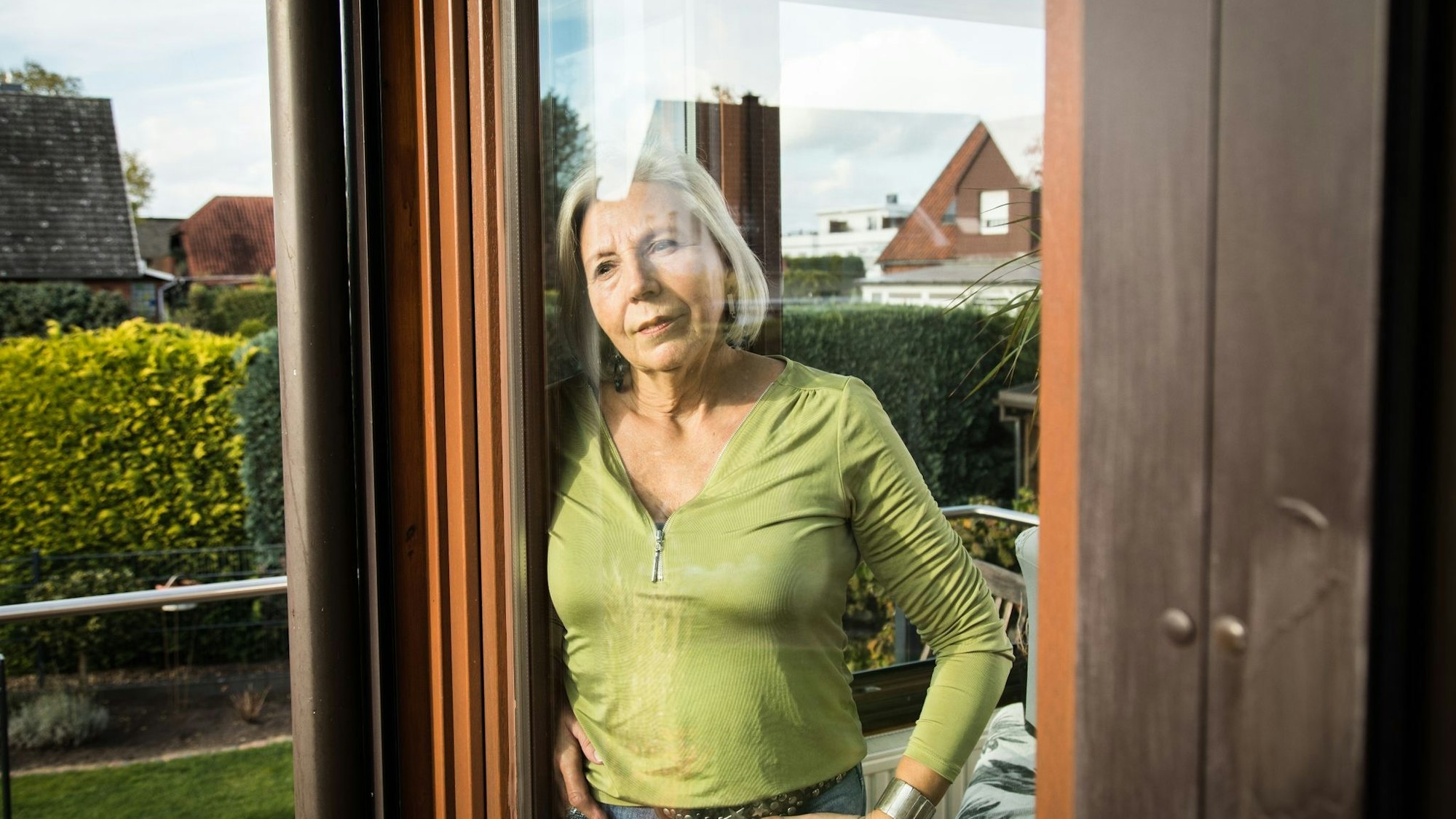 Eine Frau steht in ihren Haus und blickt durch die Fensterscheibe in ihren Garten.
