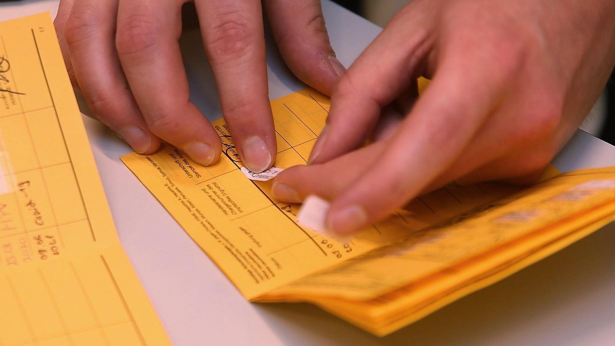 Ein Nachweis über eine Corona-Schutzimpfung wird in ein Impfbuch geklebt.