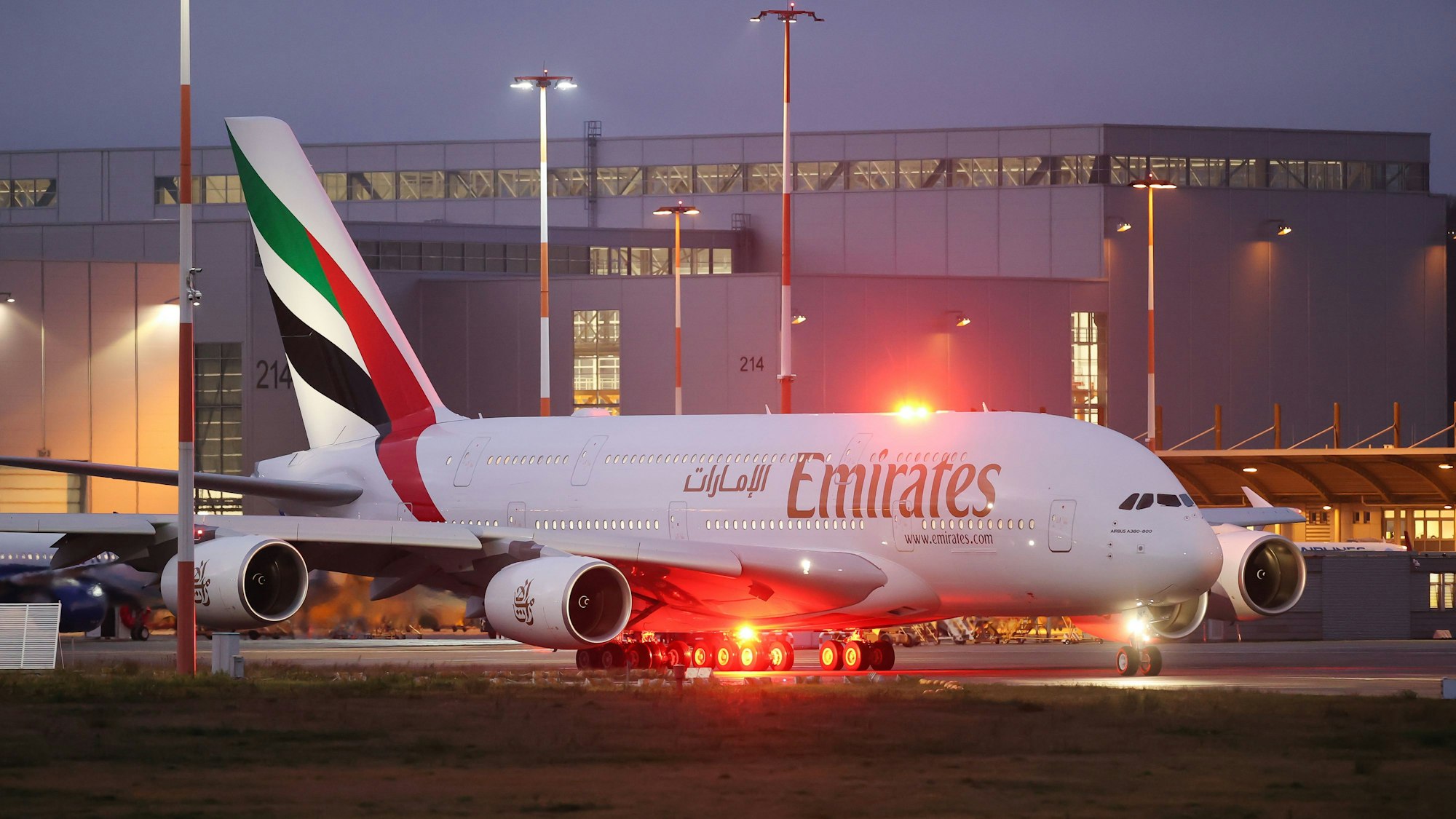 Ein Airbus A380 der arabischen Fluggesellschaft Emirates rollt zur Start- und Landebahn. Im Hintergrund ist ein großer Hangar zu sehen.