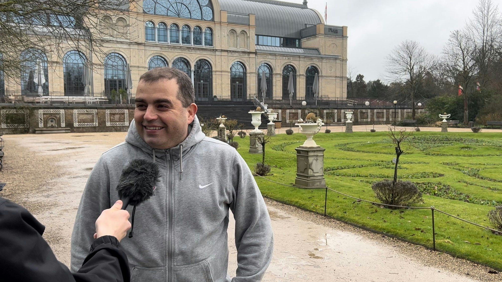 Ein Mann mit grauer Jacke steht in einem Park.