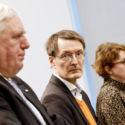 Links steht Laumann bei einer Pressekonderenz, sein Bild ist leicht verschwommen. Lauterbach steht rechts daneben, die Kamera fokussiert auf ihn. Lauterbach blickt auf Laumann.