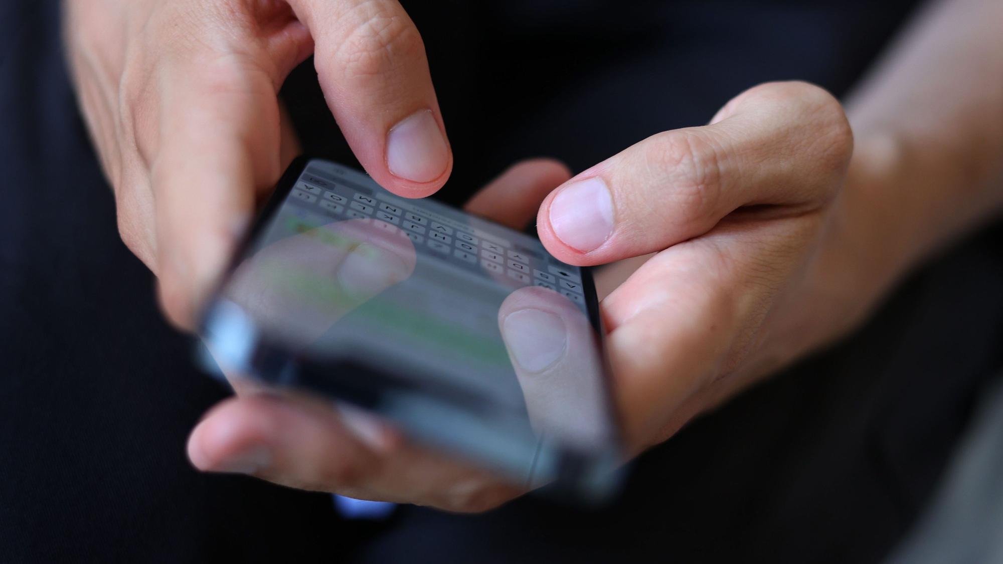 Ein junger Mann tippt auf einem Smartphone eine WhatsApp Nachricht.